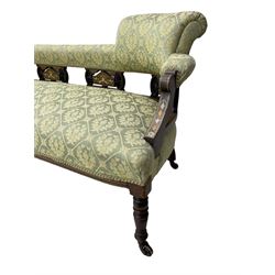 Late Victorian walnut salon settee or chaise lounge, double-ended with rolled back and curved end, upholstered in light aquamarine fabric with raised repeating lozenge pattern, decorated with laurel leaf wreaths and urns, three pierced splats carved with curled leaves, inlaid with dolphins and scrolled foliate motifs in simulated ivory and boxwood, on tapering ring turned supports with brass and ceramic castors (L166, D60, H70cm); together with matching tub-shaped armchair (W61cm, H73cm, D66cm)  