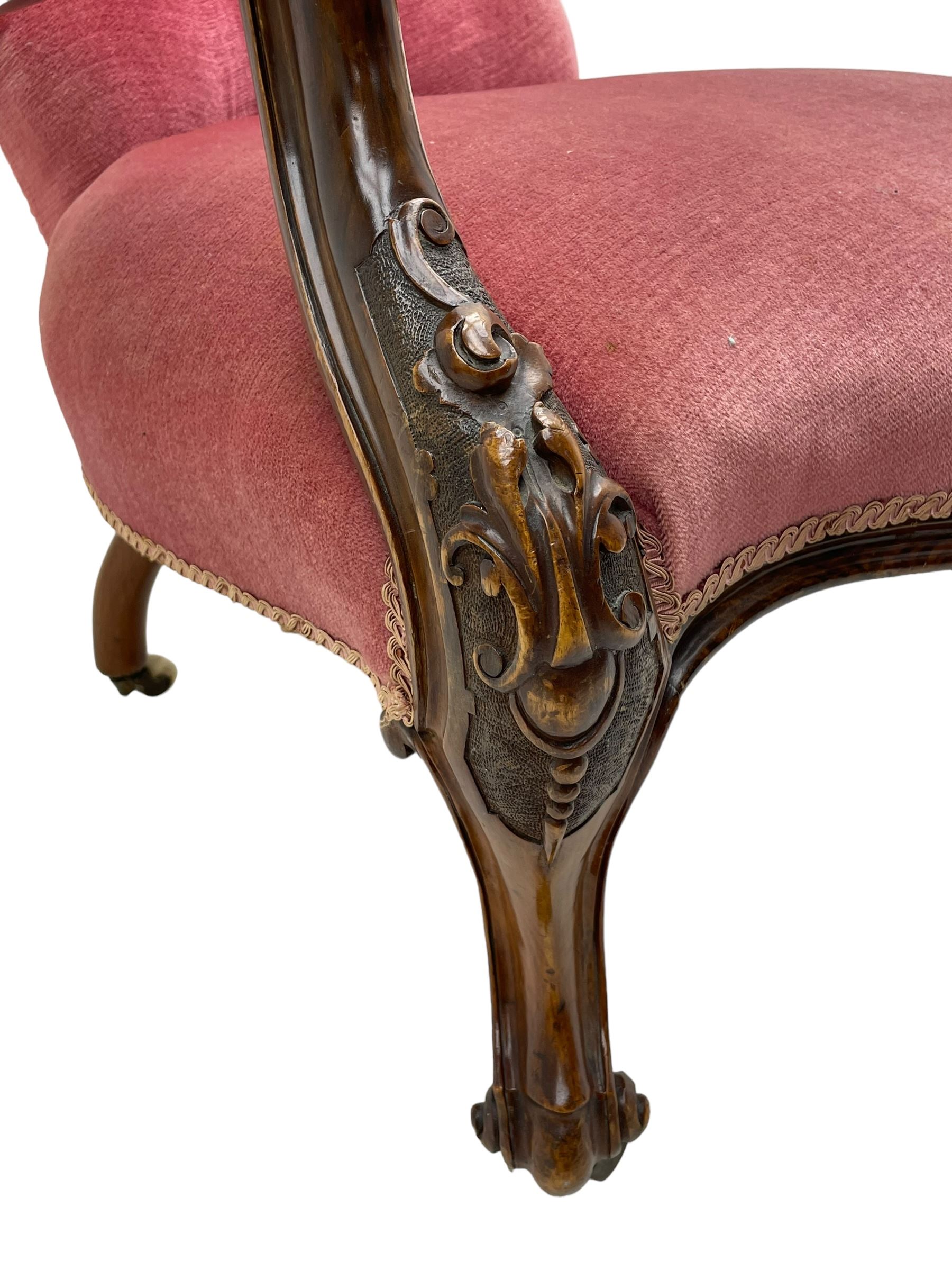 Victorian carved walnut open armchair, foliate carved cresting rail over butted back and sprung seat, upholstered in pink velvet scrolled arm terminals with moulded scrolling vines terminating to cabriole supports and ceramic castors