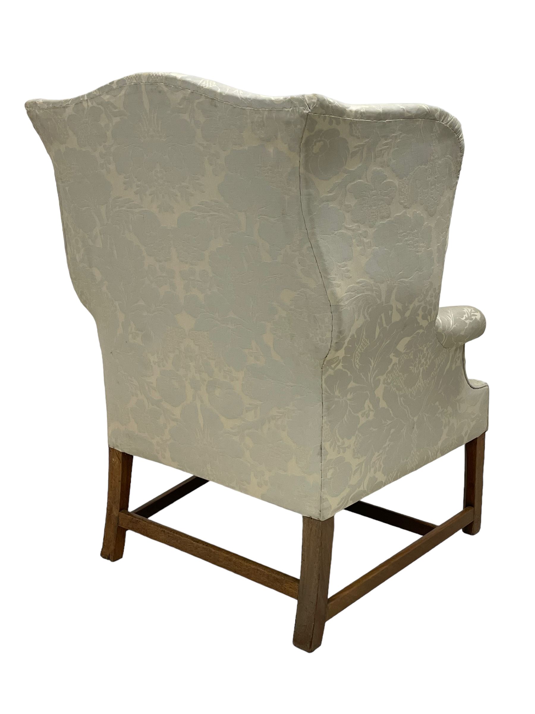 Georgian mahogany framed wingback armchair, upholstered in floral pattern silk damask fabric, wide seat enclosed by rolled arms, on chamfered square supports united by plain stretchers 