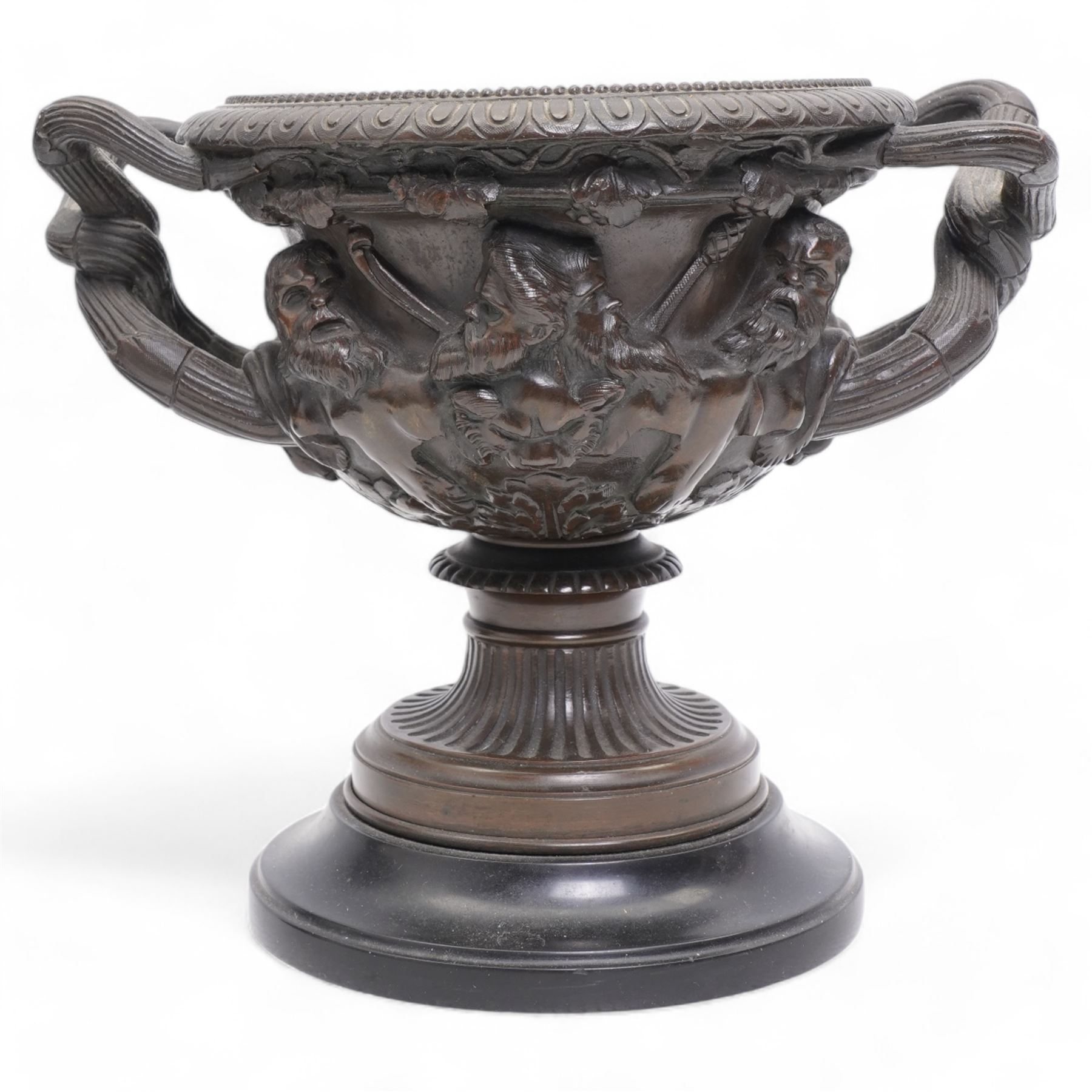 Pair of 19th/ early 20th century bronze 'Warwick' vases, after the antique, of typical form, cast with Bacchic masks and Thyrsus, on a lion pelt-cast ground, with egg and dart and beaded borders and twin reeded bifurcated branch handles, on square marble plinths, H17cm x W20cm