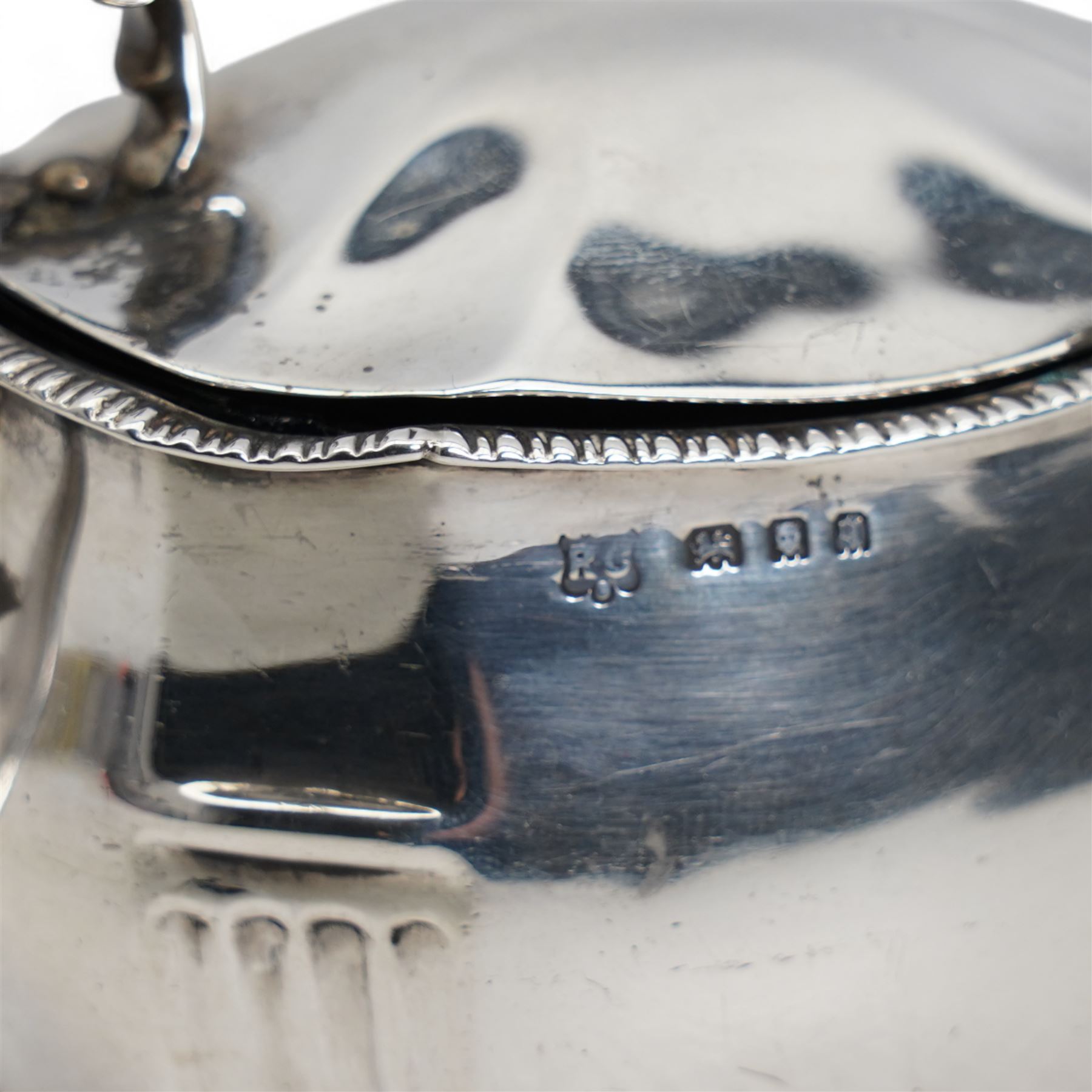 George III silver cream jug with later embossed decoration London 1797 Maker Thomas Meriton and a silver mustard pot with blue glass liner London 1931 Maker William Comyns & Sons Ltd (2)