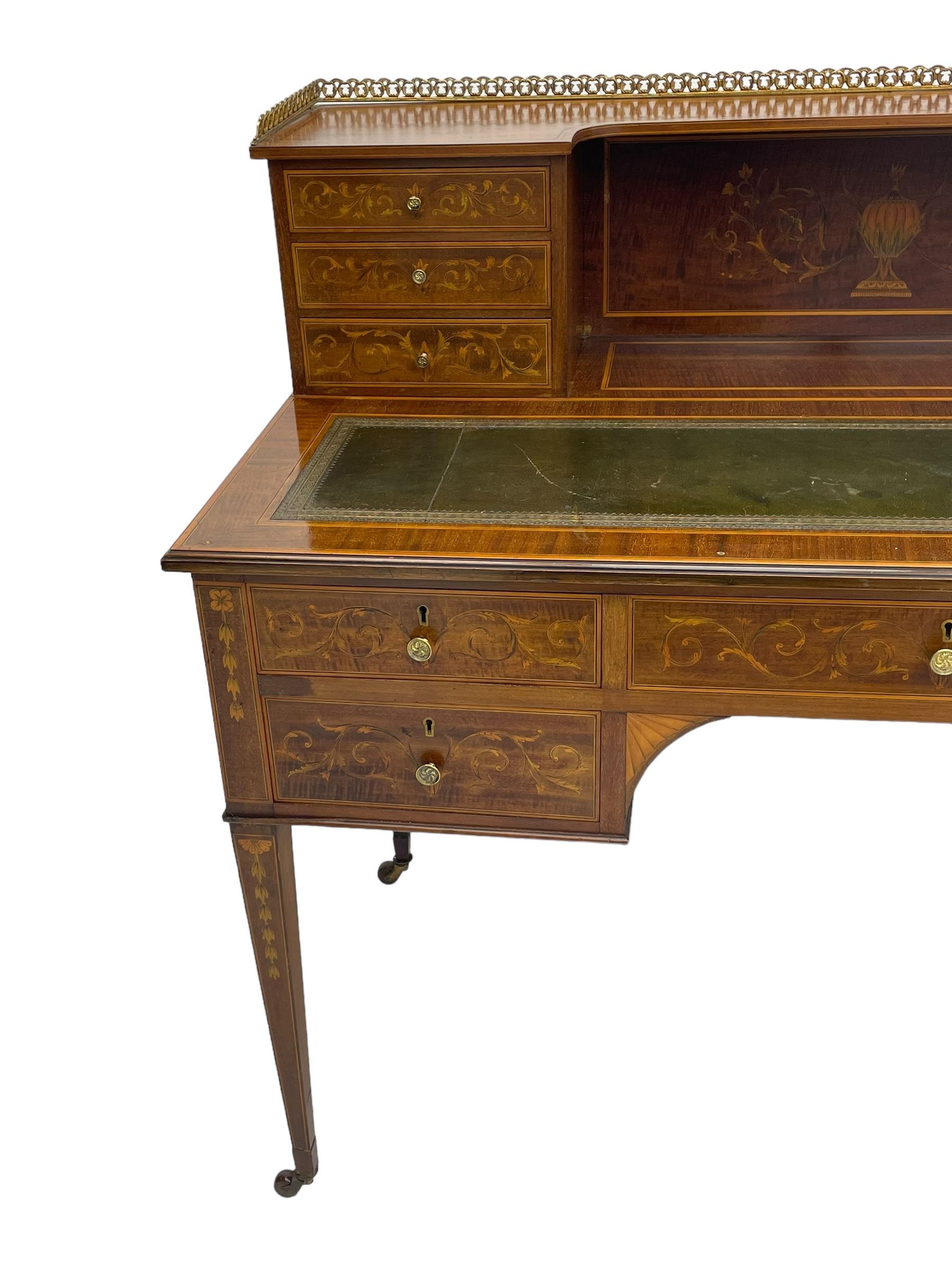 Edwardian inlaid mahogany writing desk, raised galleried back over inlaid central urn with scrolling leafy branches and six small drawers, satinwood banded rectangular moulded top with tooled leather inset, fitted with five drawers, the drawer facias inlaid with scrolling foliage and satinwood banding, square tapering supports inlaid with trailing bell flowers, on brass and ceramic castors 