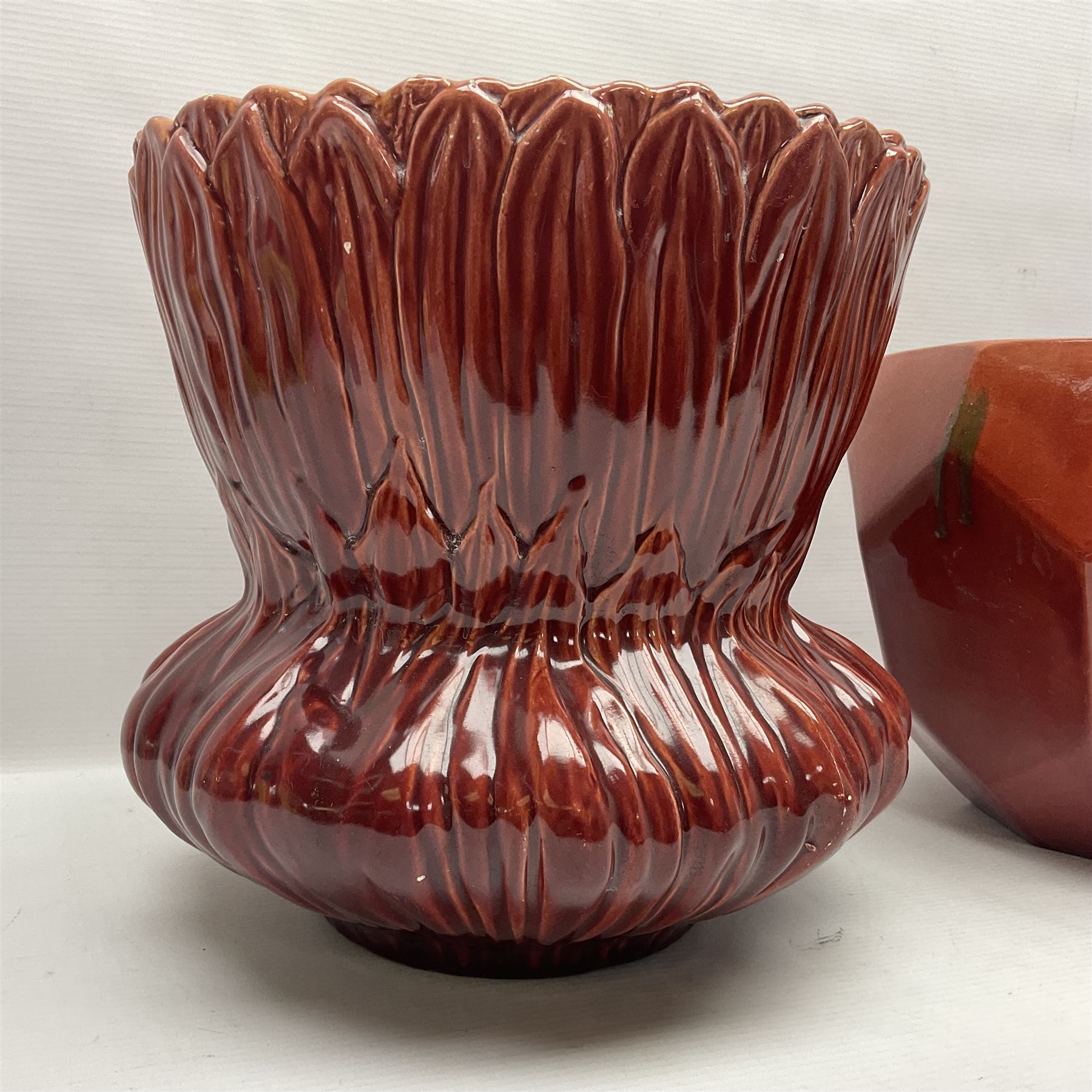 Two Bretby jardinieres, the first example with geometric hexagonal decoration in a red glaze, the second moulded as a flower head, in red glaze with yellow glaze to interior,  both with impressed marks beneath, tallest H25.5cm