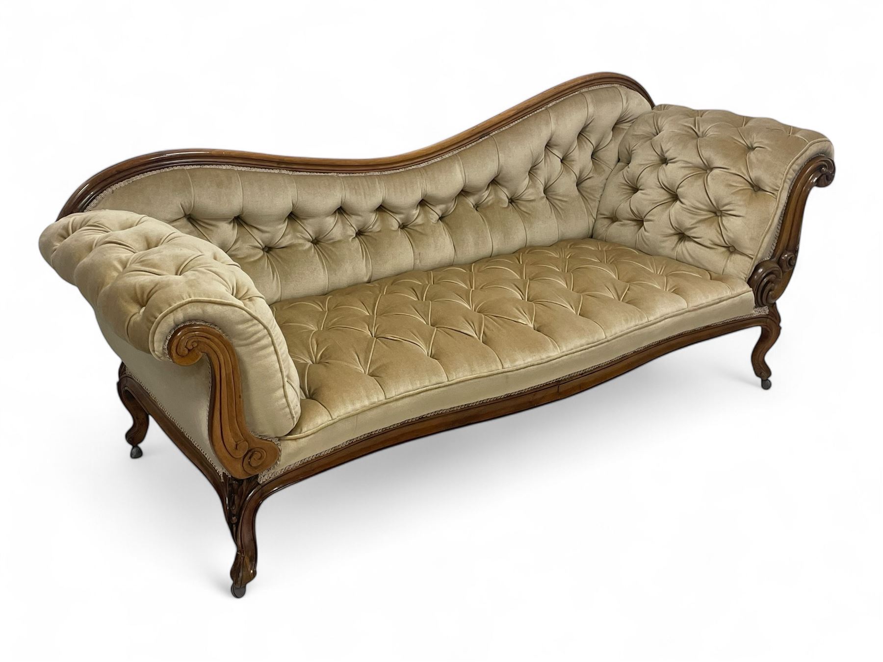 19th century walnut framed chaise longue, shaped back over scrolled arms decorated with moulded curling acanthus carvings, upholstered in deep buttoned champagne fabric, raised on cabriole supports with applied floral carved decoration, on castors