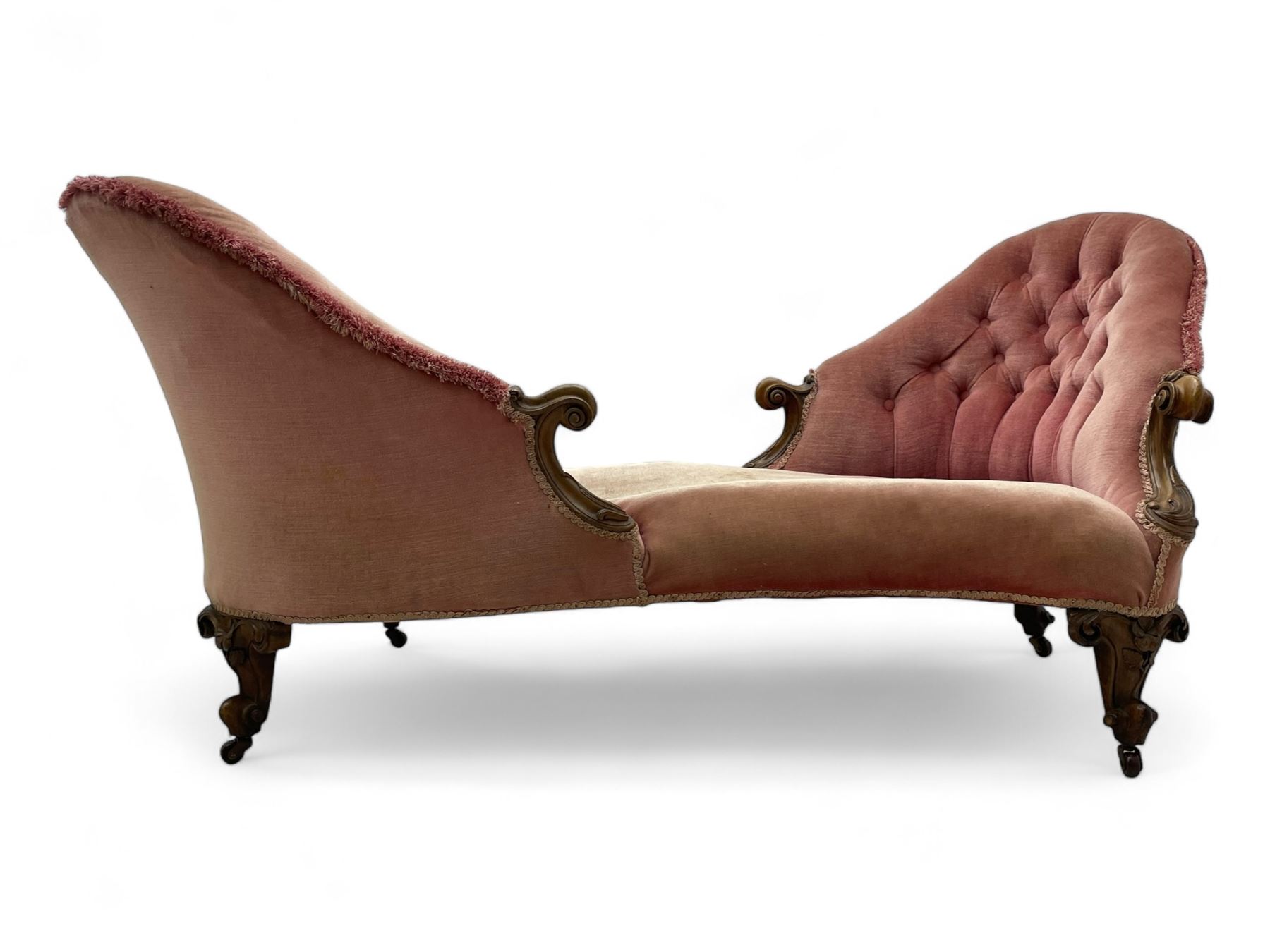 Victorian walnut framed tete-a-tete loveseat, scrolled arm terminals with moulded foliate decoration, buttoned backs and sprung seat upholstered in pale pink velvet, raised on cabriole supports with applied flower heads and scroll feet terminating to ceramic castors