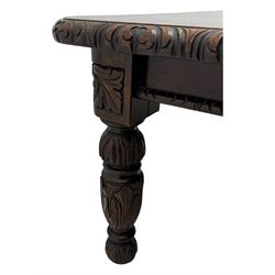 19th century heavily carved oak extending dining table, rectangular top with rounded corners and carved gadrooned edge, extending via winding mechanism with two additional leaves, raised on acanthus leaf-carved baluster supports terminating in ceramic castors