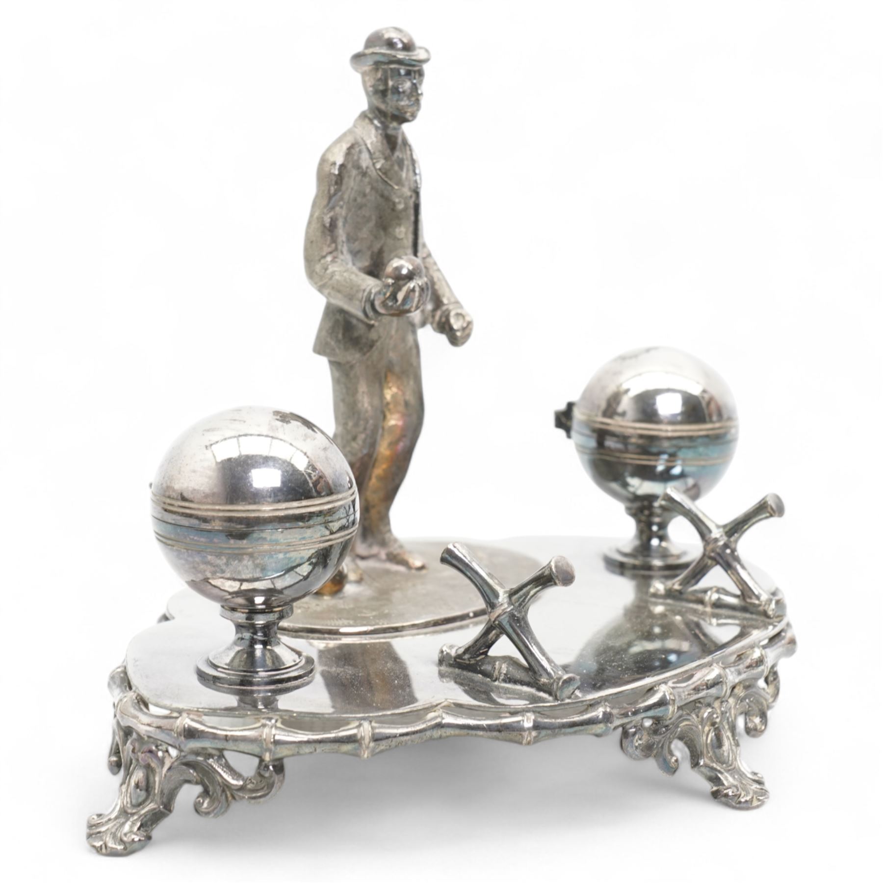 Victorian silver-plated inkstand by James Dixon & Sons, the quatrefoil base surmounted with a figure of a lawn bowler stood upon an oval grass base, with three lawn bowls by his feet, the inkwells formed as two bowls, each with hinged covers and silver-plated liners, bamboo moulded pen rest and gallery, supported by four pierced and splayed feet, L22cm x H17cm