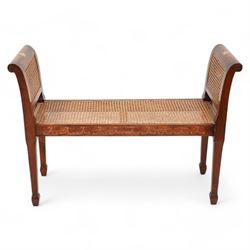 Regency design mahogany window seat, rolled uprights terminating to tapering supports with spade feet, cane work seat enclosed by double caned sides, with floral and C-scroll painted decoration 