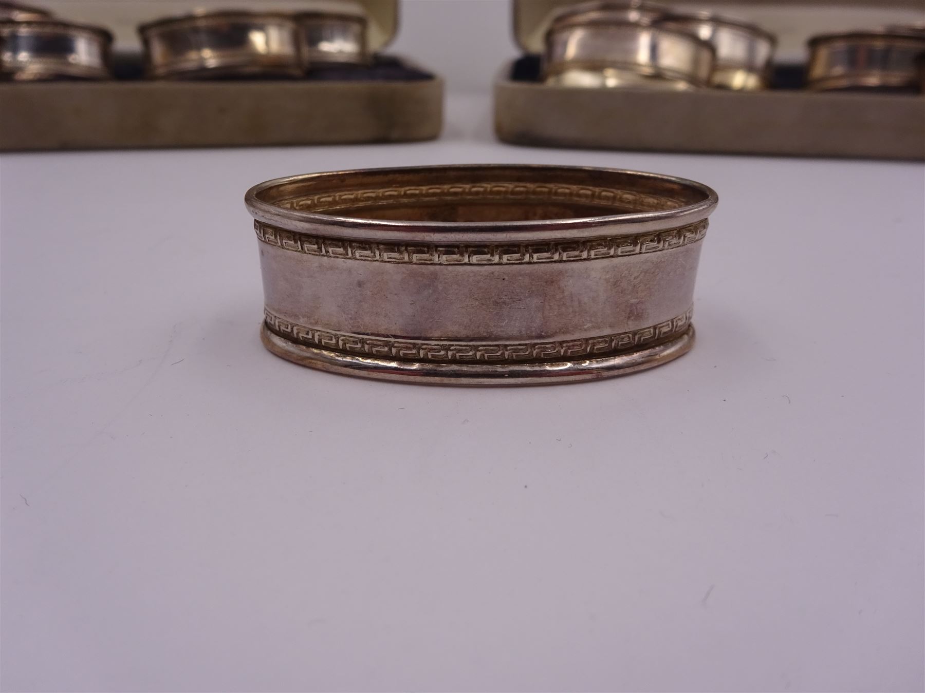 Two sets of six modern silver napkin rings, each of oval form, with Greek key decoration, hallmarked Ari D Norman, London 1986, both in fitted cases