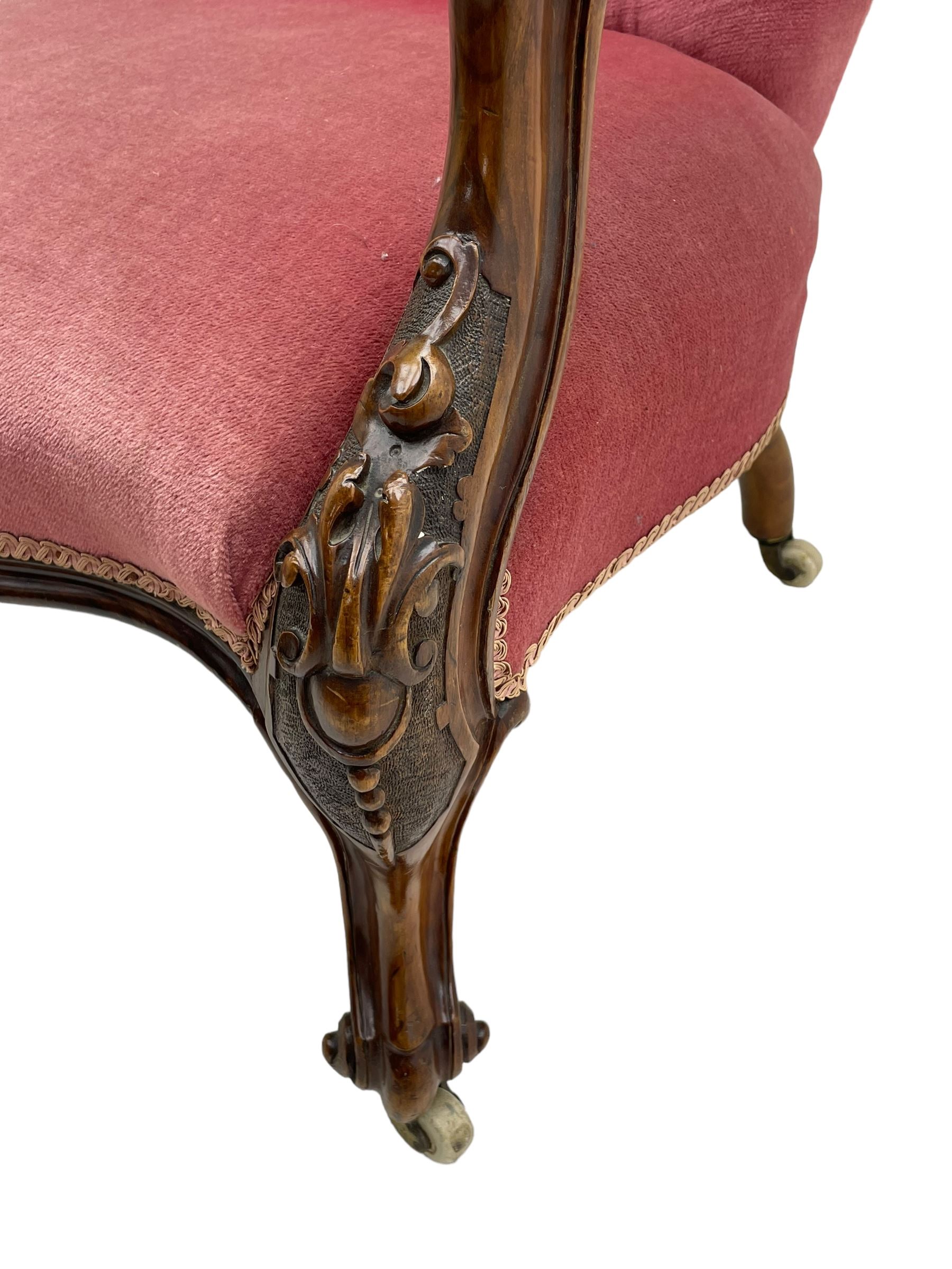 Victorian carved walnut open armchair, foliate carved cresting rail over butted back and sprung seat, upholstered in pink velvet scrolled arm terminals with moulded scrolling vines terminating to cabriole supports and ceramic castors