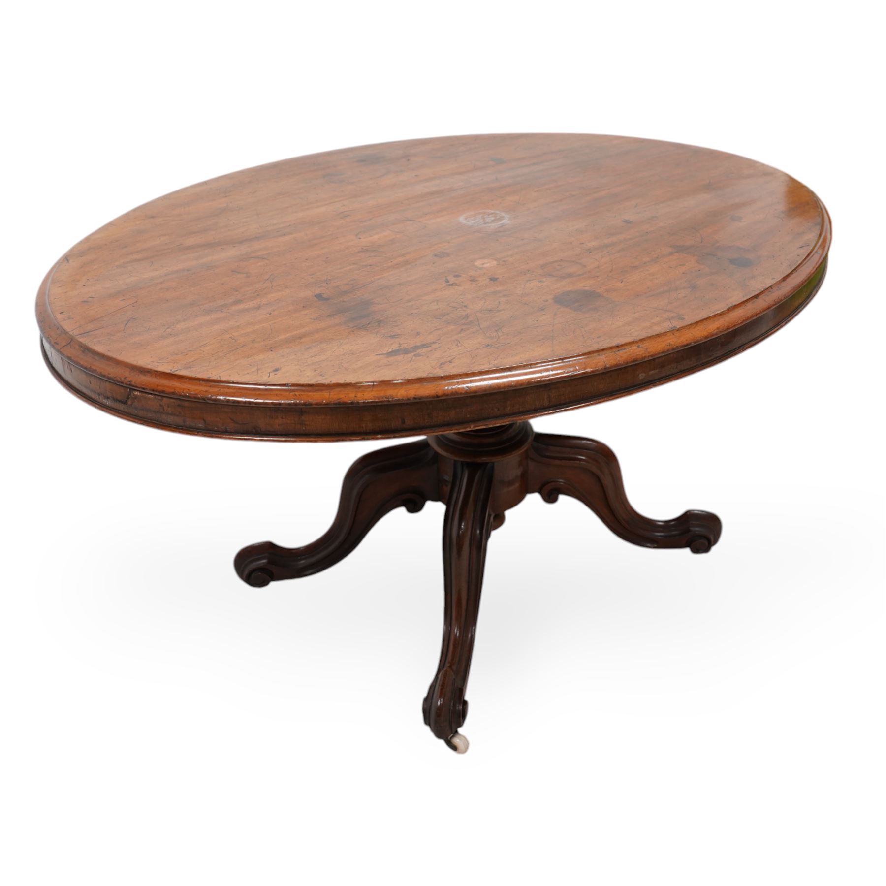 Victorian mahogany loo or centre table, moulded oval tilt-top, turned pedestal on four out splayed carved supports with scrolled terminals, on brass and ceramic castors 