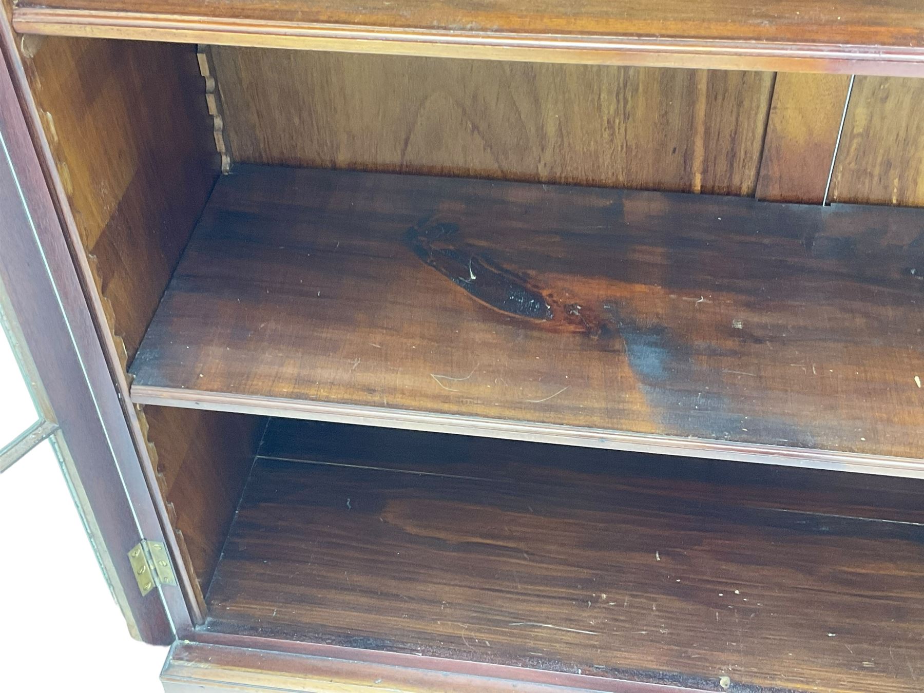 Early 20th century mahogany bookcase, projecting dentil cornice over blind fretwork frieze, enclosed by two astragal glazed doors, on shaped bracket feet 