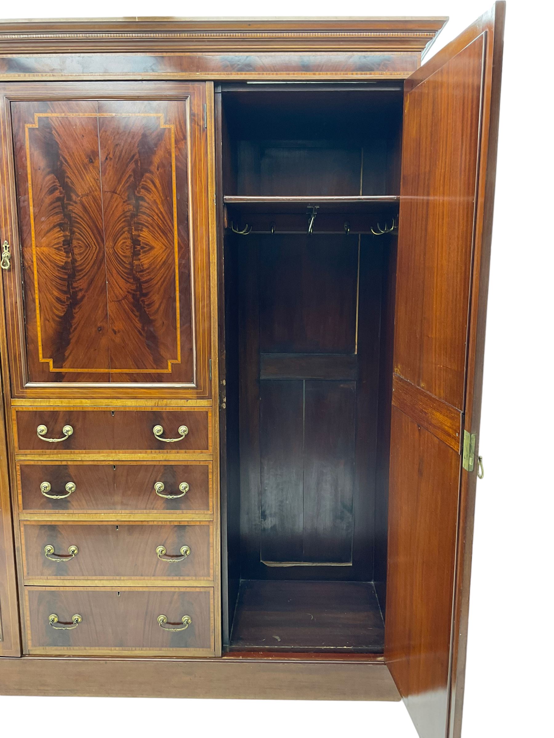 Edwardian inlaid mahogany combination wardrobe, projecting moulded cornice over figured frieze with satinwood banding, the central section fitted with cupboard over four long drawers, figured matched veneers and satinwood bands, flanked by two full height compartments enclosed by bevelled shield shaped mirror doors, satinwood fan inlaid spandrels, on moulded skirt base 