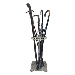 Victorian design cast iron umbrella stand, ornate stem on shell C-scroll base; together with a collection of walking sticks including a silver tipped cane 