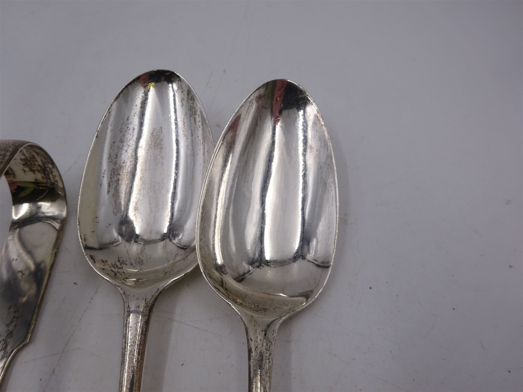 Two George III silver table spoons, including a bottom struck Hanoverian pattern example, hallmarked Thomas Dene, London 1766, and a pair of silver sugar tongs, hallmarked Newcastle 1842, maker's mark TW