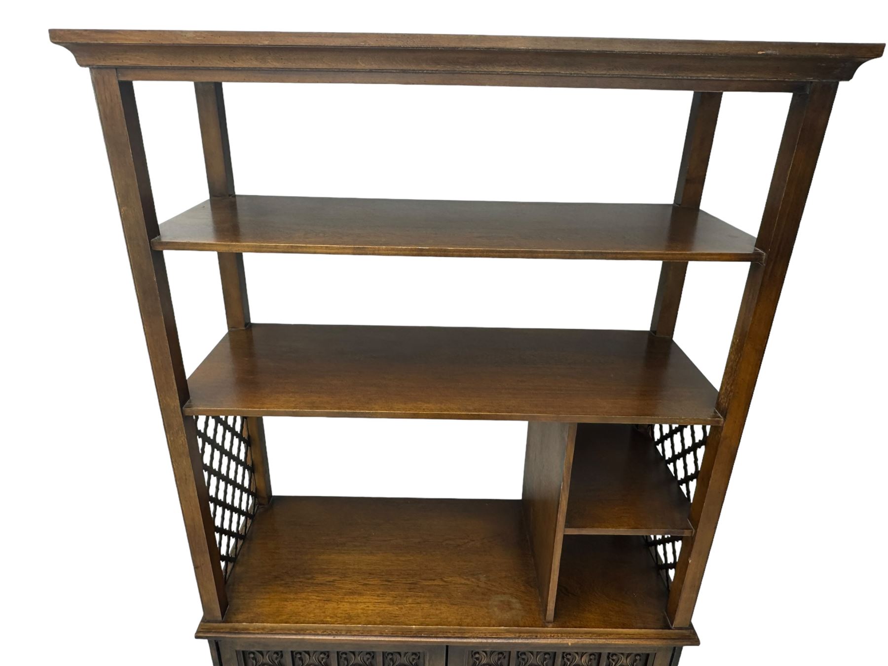 Mid 20th century oak bookcase cupboard, projecting cornice over three open shelves with subdivided sections and latticework uprights, two doors to the base with floral and scrollwork carvings and central brass handles, resting on a moulded plinth base