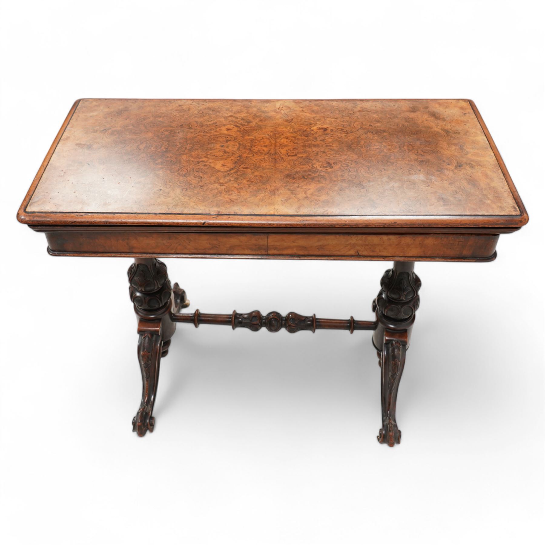 Victorian figured walnut card table, moulded rectangular fold-over swivel top with baize-lined interior, on twin turned pillar supports carved with stylised foliate motifs, united by turned stretcher, on splayed shaped feet with scrolled carved terminals, brass and ceramic castors 