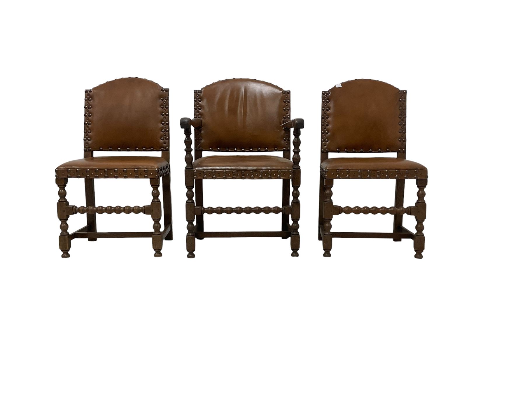 Set of six (4+2) early 20th century oak dining chairs, arched back and seat upholstered in tan leather with studwork detail, on turned supports united by bobbin-turned stretchers