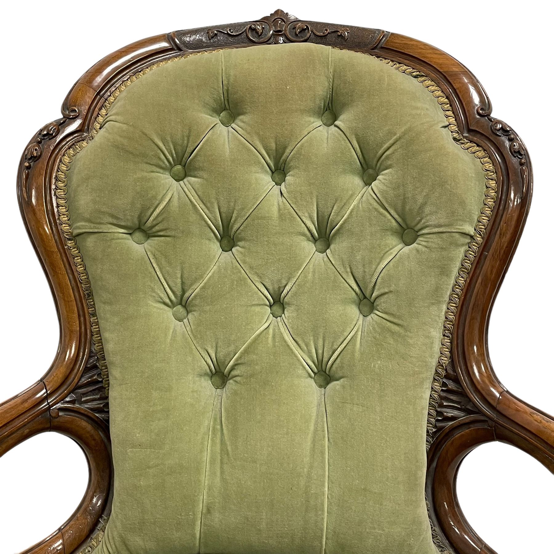 Pair of lady's and gentleman's Victorian carved walnut armchair and nursing chair, foliate carved cresting rail over shaped back with scrolled acanthus carved sides, the armchair with scroll arm terminals, the spoon back and sprung seat upholstered in buttoned sage green velvet, raised on cabriole supports with bell-flower moulded knees and scroll feet, on ceramic castors