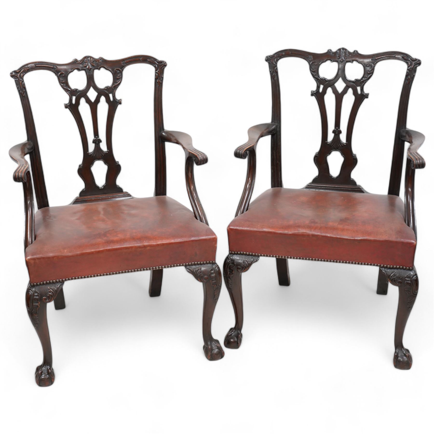 Early 20th century pair of Chippendale design mahogany elbow chairs, shaped cresting rail carved with foliate cartouches and scrolled leaves, pierced and interlaced Gothic splat, shaped arms with scroll carved terminals, leather upholstered seat with stud band, cartouche carved cabriole supports with ball and claw feet 