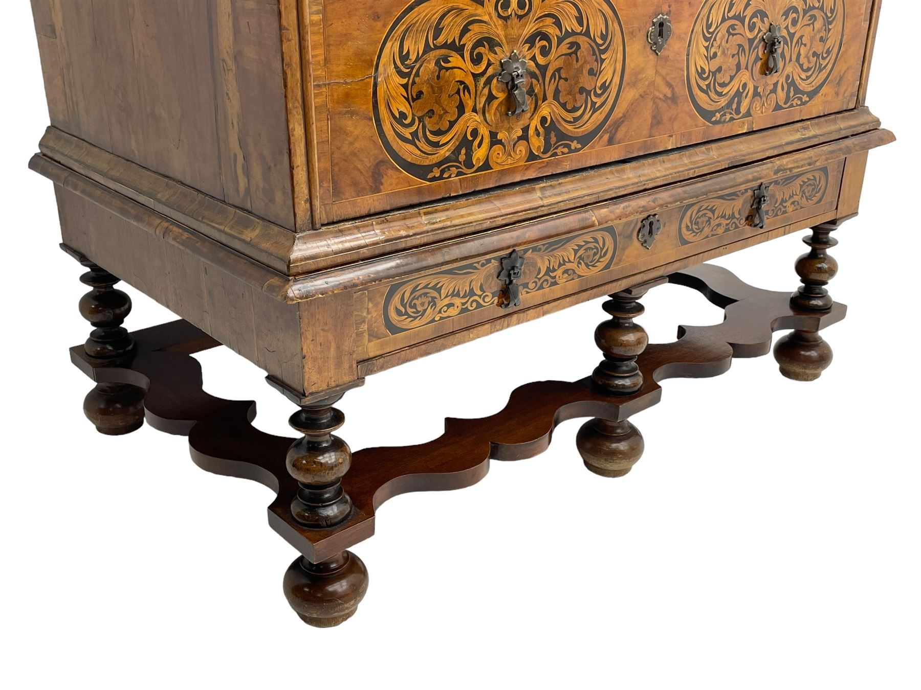 18th century inlaid walnut chest on stand, ovolo-moulded rectangular top inlaid with ebony panels each decorated with scrolling foliage, flower heads and birds, fitted with two short over three long drawers, the drawer fronts decorated with ebony panels enclosing curled leaf inlays, the base fitted with single drawer on turned supports united by waved stretchers, on turned bun feet 