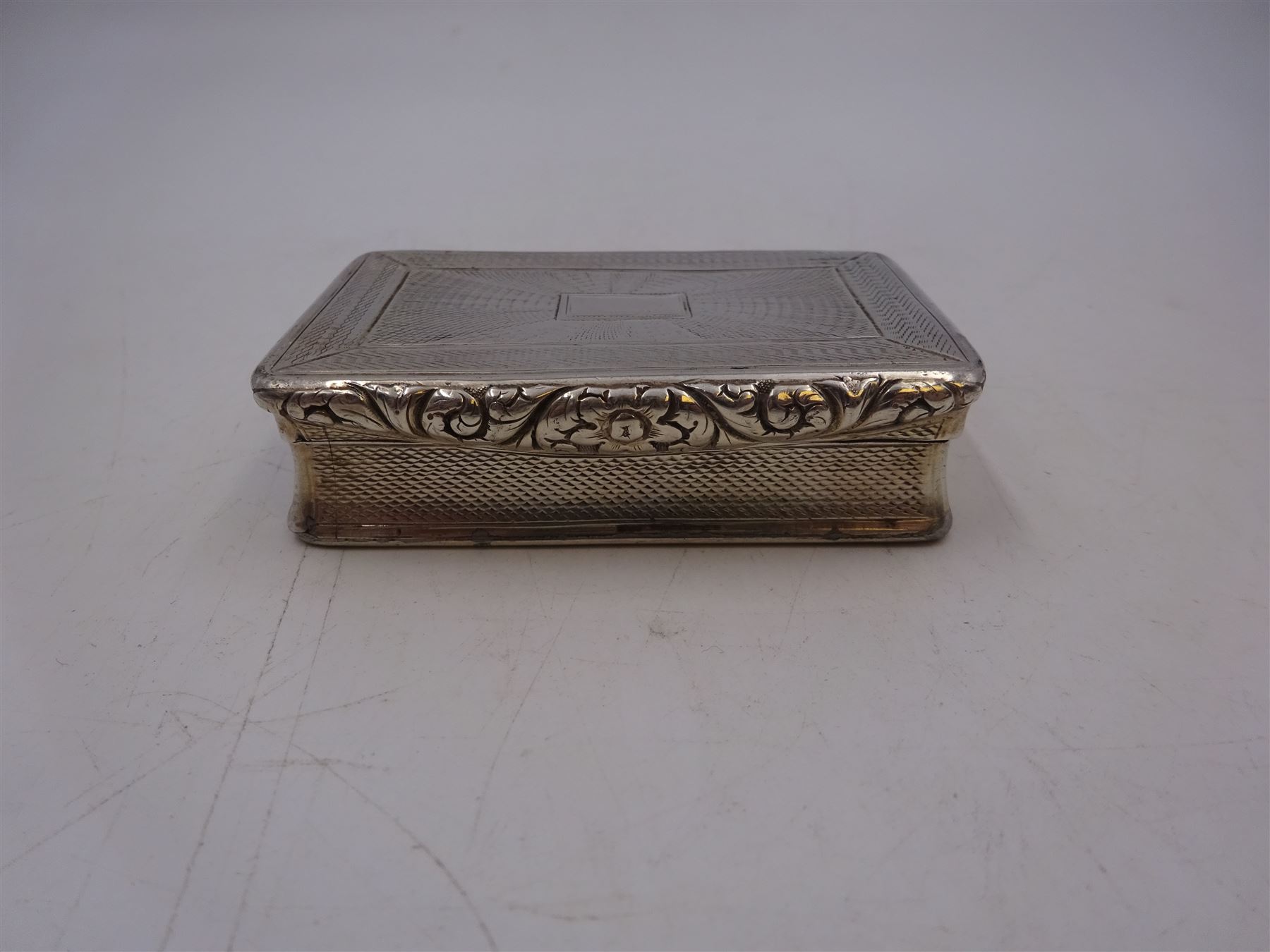 George IV silver snuff box, of rectangular form, with engine turned decoration, chased foliate borders and blank cartouche to centre of hinged cover, opening to reveal a gilt interior, hallmarked John Bettridge, Birmingham 1825, W7.6cm