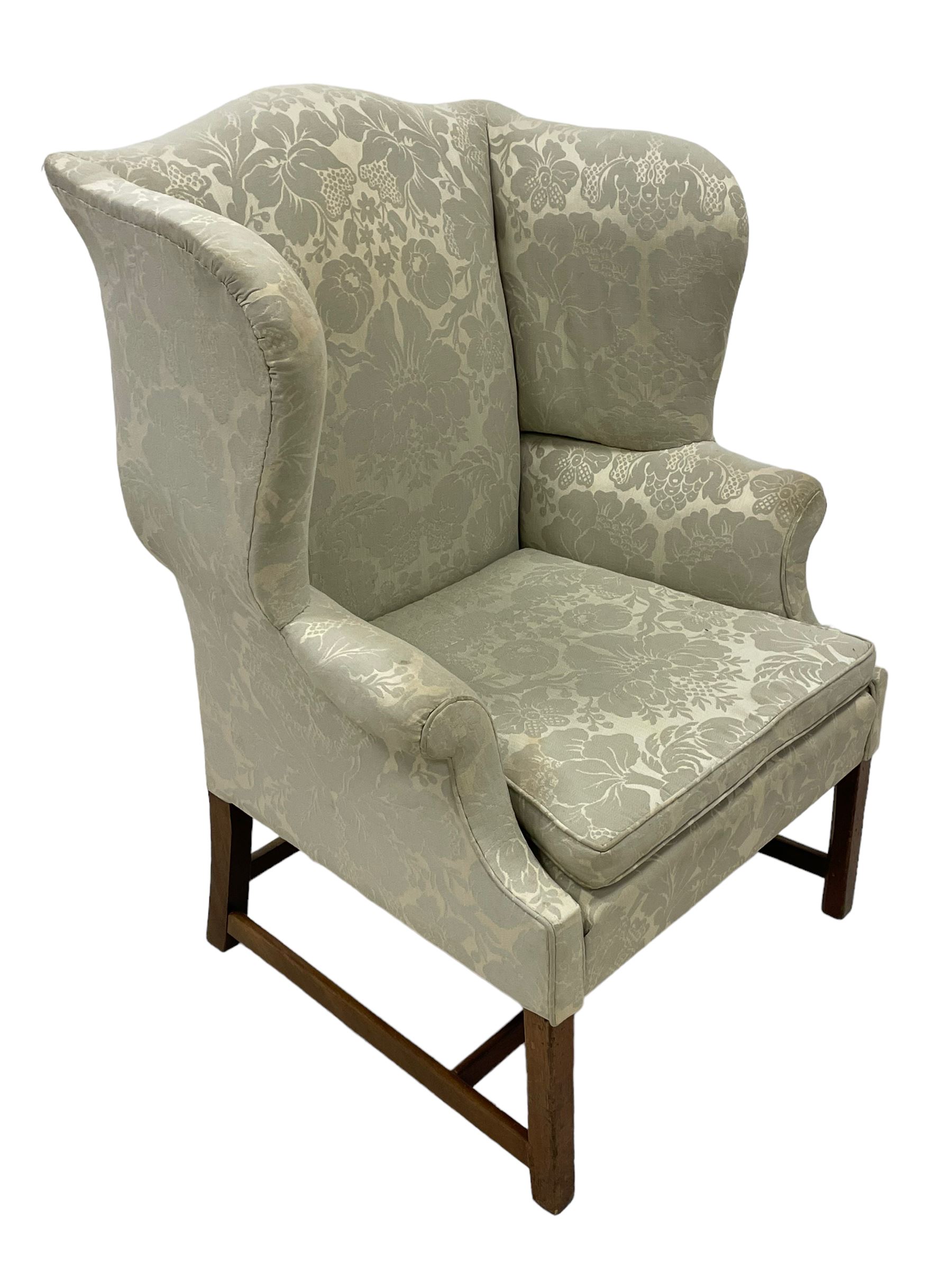 Georgian mahogany framed wingback armchair, upholstered in floral pattern silk damask fabric, wide seat enclosed by rolled arms, on chamfered square supports united by plain stretchers 