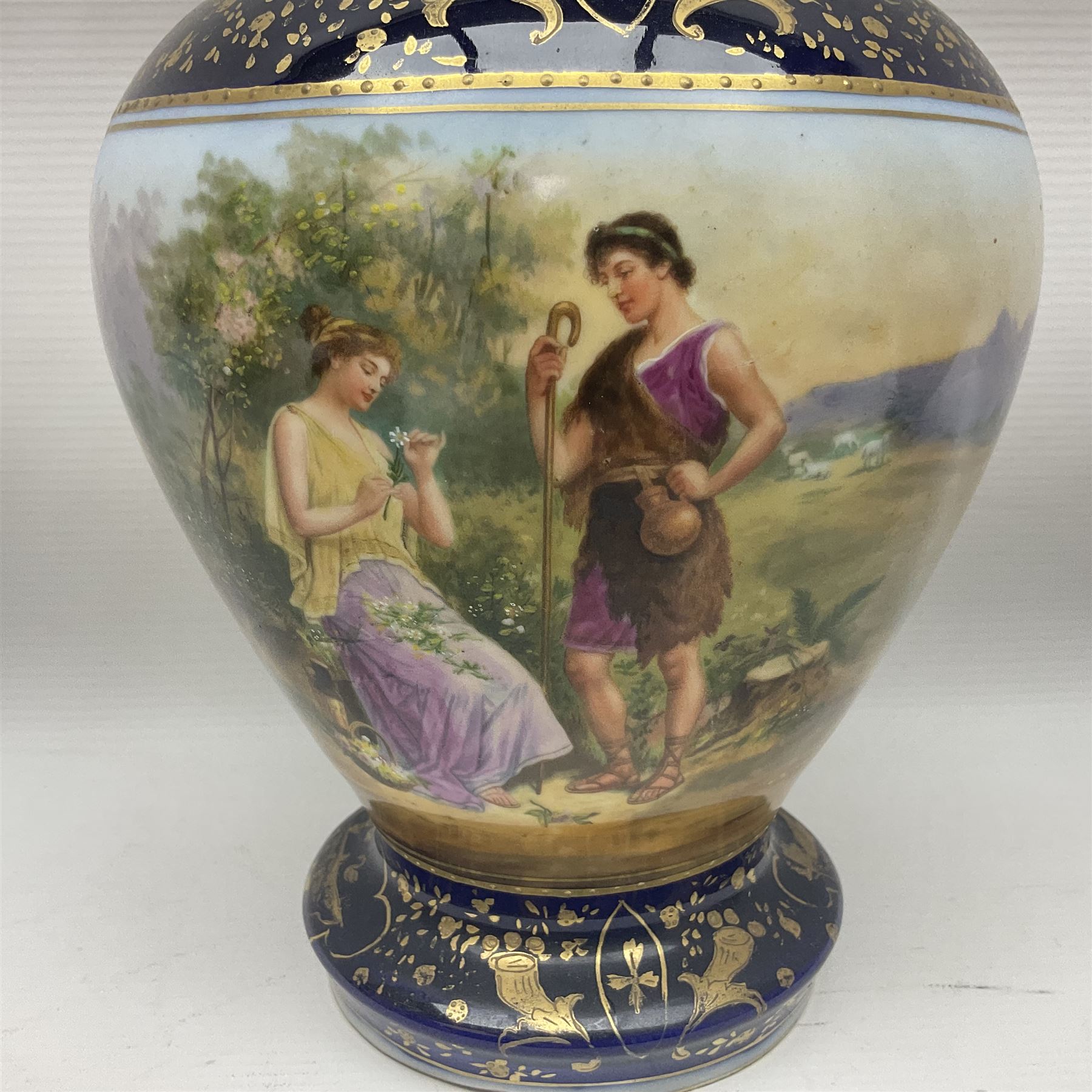 19th century Vienna style porcelain 'Musik' garniture, the central vase of baluster form with domed cover flanked by two smaller vases with twin curved gilt handles to short neck, each decorated with classical figural vignettes between blue borders heightened with gilt, H33.5cm