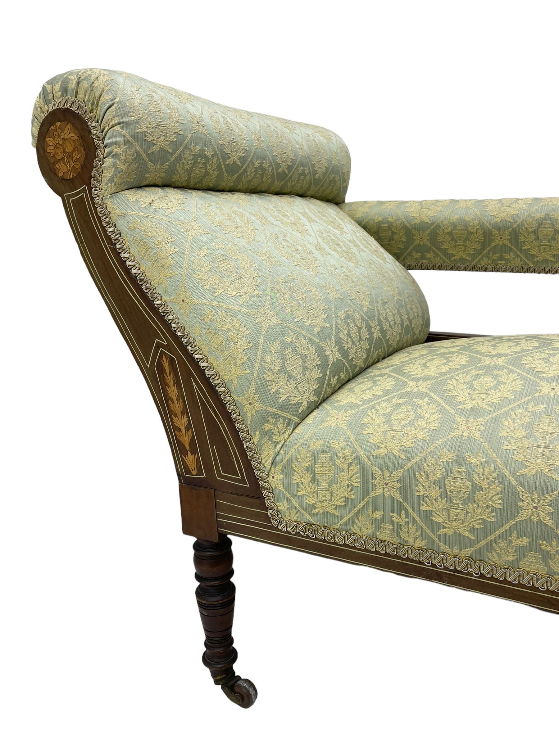 Late Victorian walnut salon settee or chaise lounge, double-ended with rolled back and curved end, upholstered in light aquamarine fabric with raised repeating lozenge pattern, decorated with laurel leaf wreaths and urns, three pierced splats carved with curled leaves, inlaid with dolphins and scrolled foliate motifs in simulated ivory and boxwood, on tapering ring turned supports with brass and ceramic castors (L166, D60, H70cm); together with matching tub-shaped armchair (W61cm, H73cm, D66cm)  