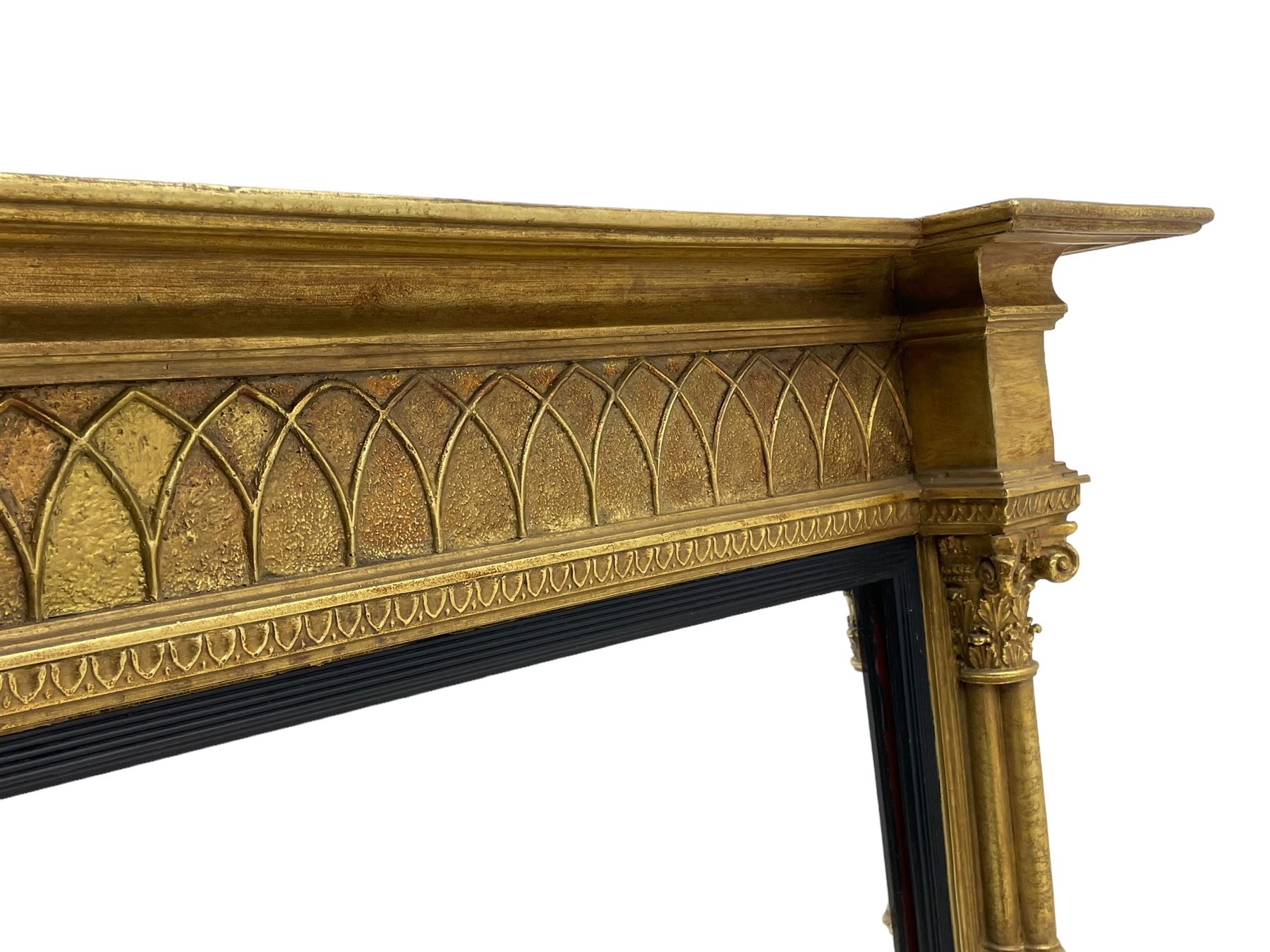 Regency design giltwood overmantel mirror, projecting cornice over pointed arcade frieze and foliate moulded upper edge, plain mirror plate within reed moulded ebonised slip, flanked by cluster columns with acanthus and scroll decorated Composite order capitals 