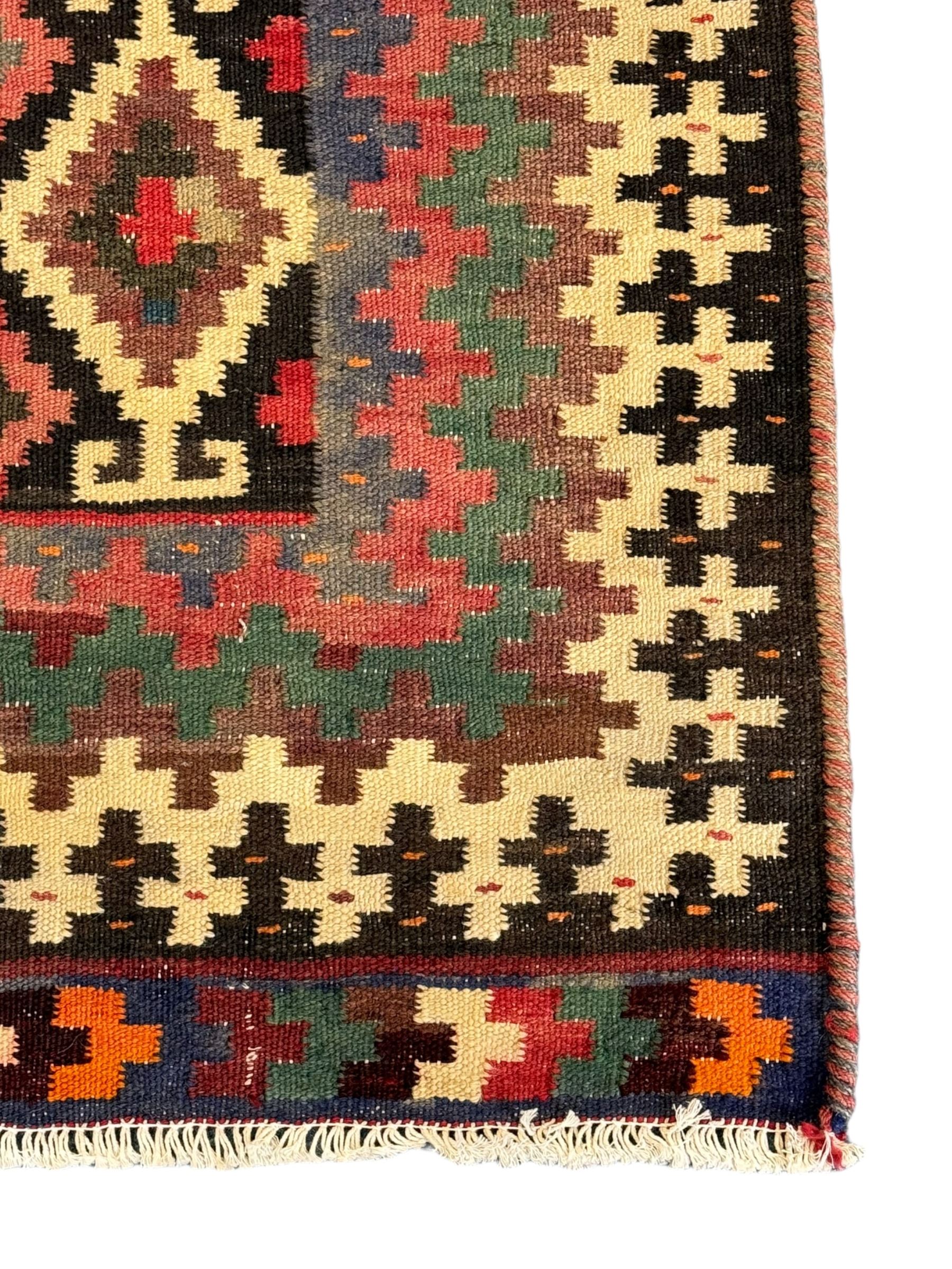 Northeast Persian Sumak Kilim red ground rug, the field decorated with rows of multicoloured diamond motifs featuring  geometric patterns, the border composed of alternating black and white stepped designs, enclosed by a narrow band with multicoloured geometric shapes