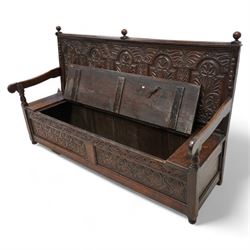 18th century oak settle or bench, moulded cresting rail with globular finials over five panel back, each stepped arch panel carved with stylised leaf decoration, hinged box seat over S-scroll foliate frieze and two panels carved with scrolling pattern, panelled sides, on stile supports terminating to turned feet 