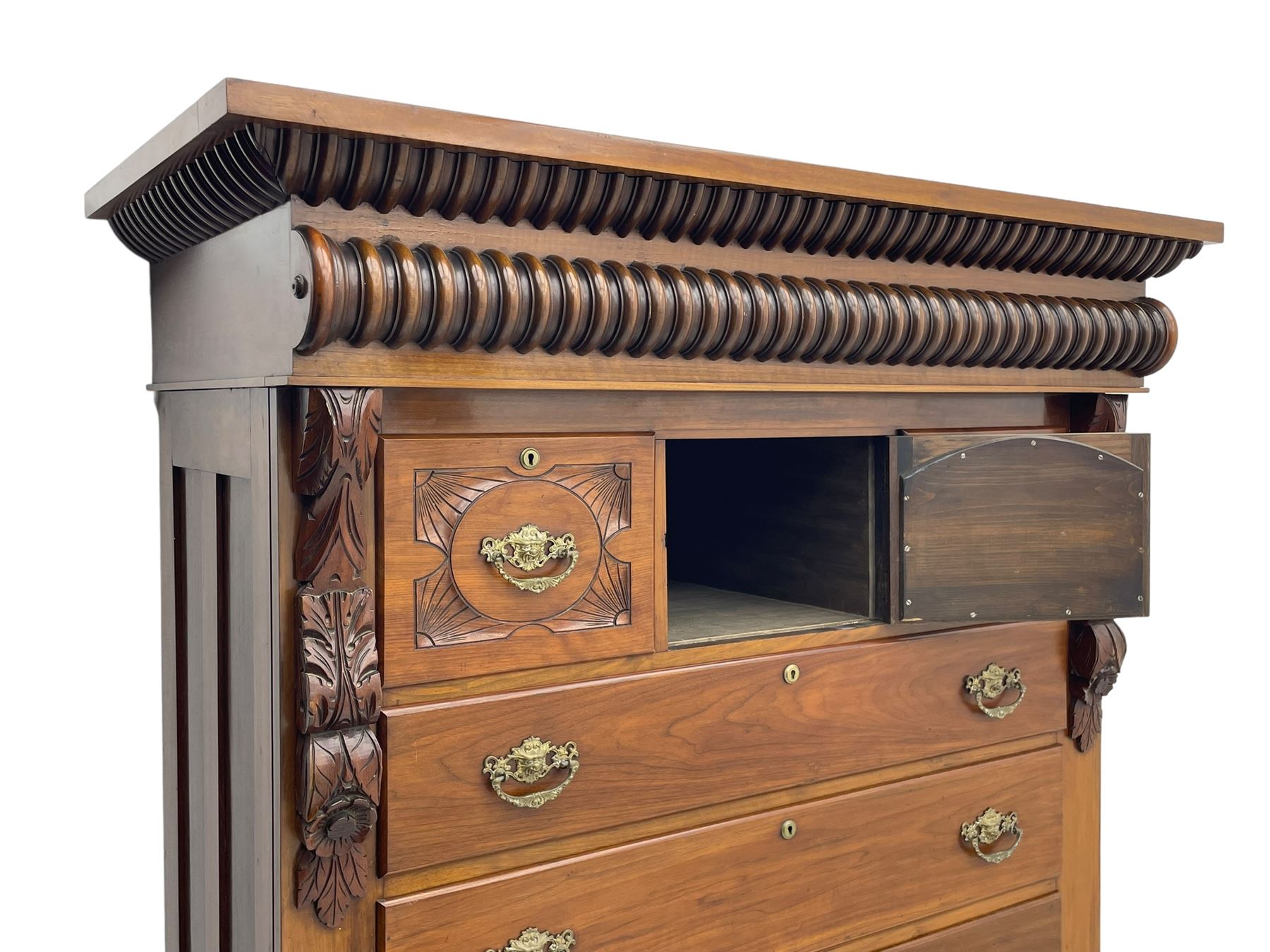 Late Victorian walnut Scotch chest, projecting cornice with turned quarter column mounts over matching half column to frieze, fitted with two upper short drawers with central cupboard, bevelled mirror glazed cupboard door, four graduating drawers below, foliage and flower head carved brackets to the uprights, panelled sides, chamfered plinth on turned feet