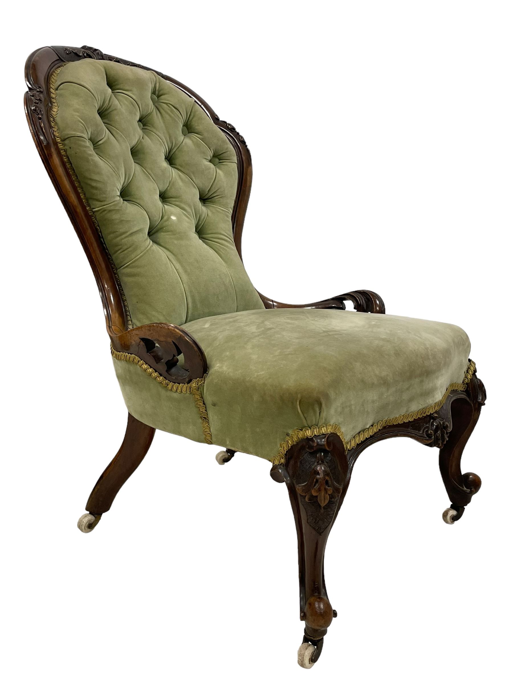 Pair of lady's and gentleman's Victorian carved walnut armchair and nursing chair, foliate carved cresting rail over shaped back with scrolled acanthus carved sides, the armchair with scroll arm terminals, the spoon back and sprung seat upholstered in buttoned sage green velvet, raised on cabriole supports with bell-flower moulded knees and scroll feet, on ceramic castors