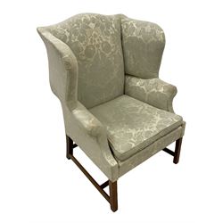 Georgian mahogany framed wingback armchair, upholstered in floral pattern silk damask fabric, wide seat enclosed by rolled arms, on chamfered square supports united by plain stretchers 