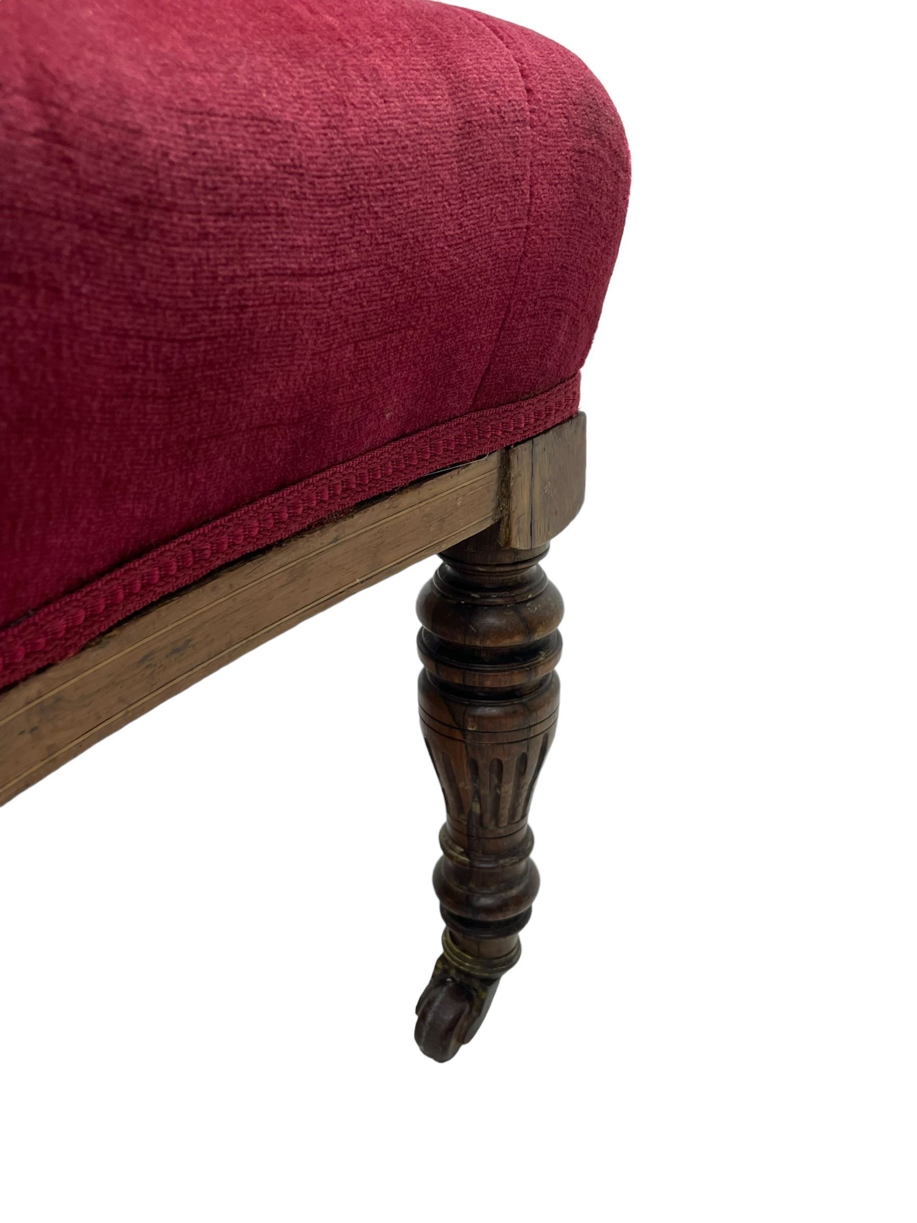 Late Victorian inlaid walnut two seat settee, the shaped cresting rail decorated with foliate inlays and boxwood stringing, upholstered in crimson velvet with sprung seat, raised on turned and fluted supports with ceramic castors