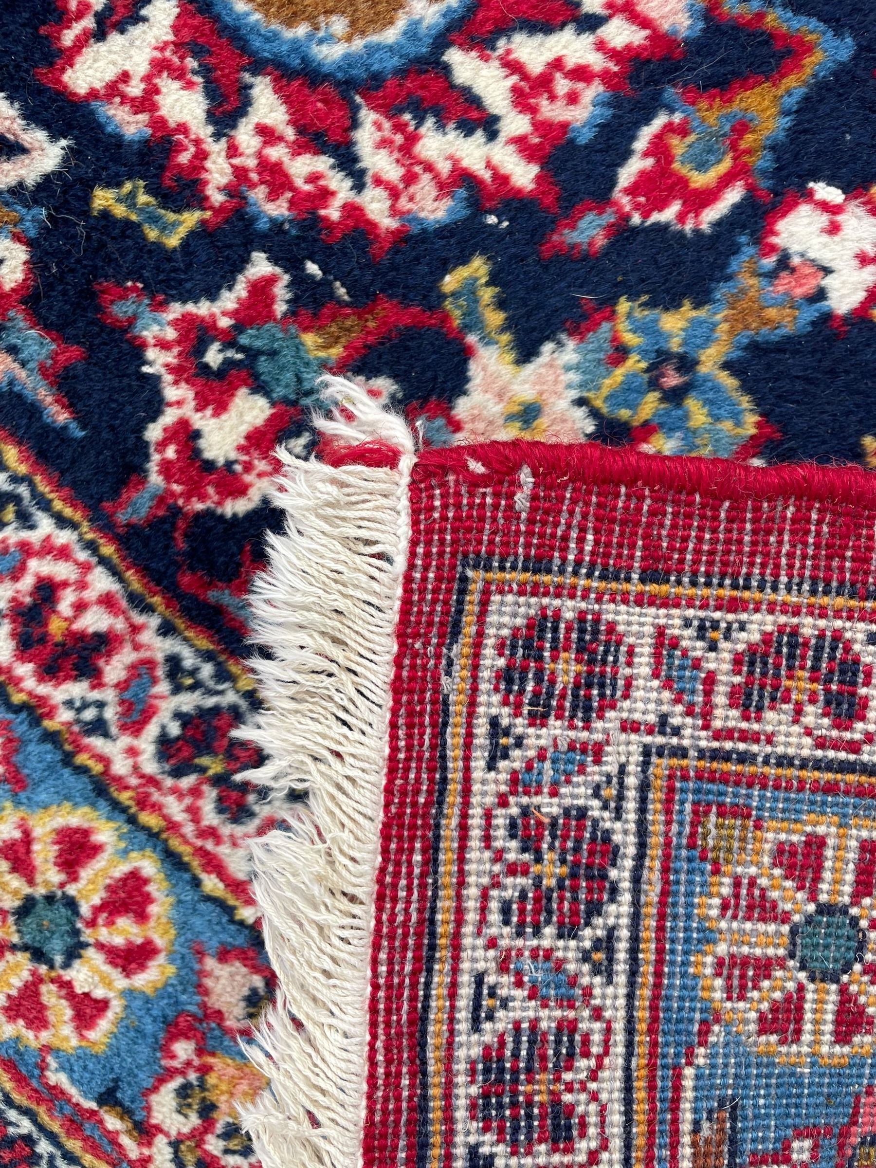 Large Persian Kashan crimson ground carpet, central floral medallion surrounded by swirling leafy branches and palmettes, enclose by floral pattern spandrels, the indigo border with overall scrolling design decorated with palmettes, within guard stripes 