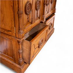 19th century pitch pine ecclesiastical vestment wardrobe or sacristy cabinet, crenelated and projecting moulded cornice over two panelled doors, the panelled doors carved with linen folds and mounted with rows of roundels depicting crucifixes and flower heads, enclosed by turned pilasters, two drawers to the base, on moulded plinth base 