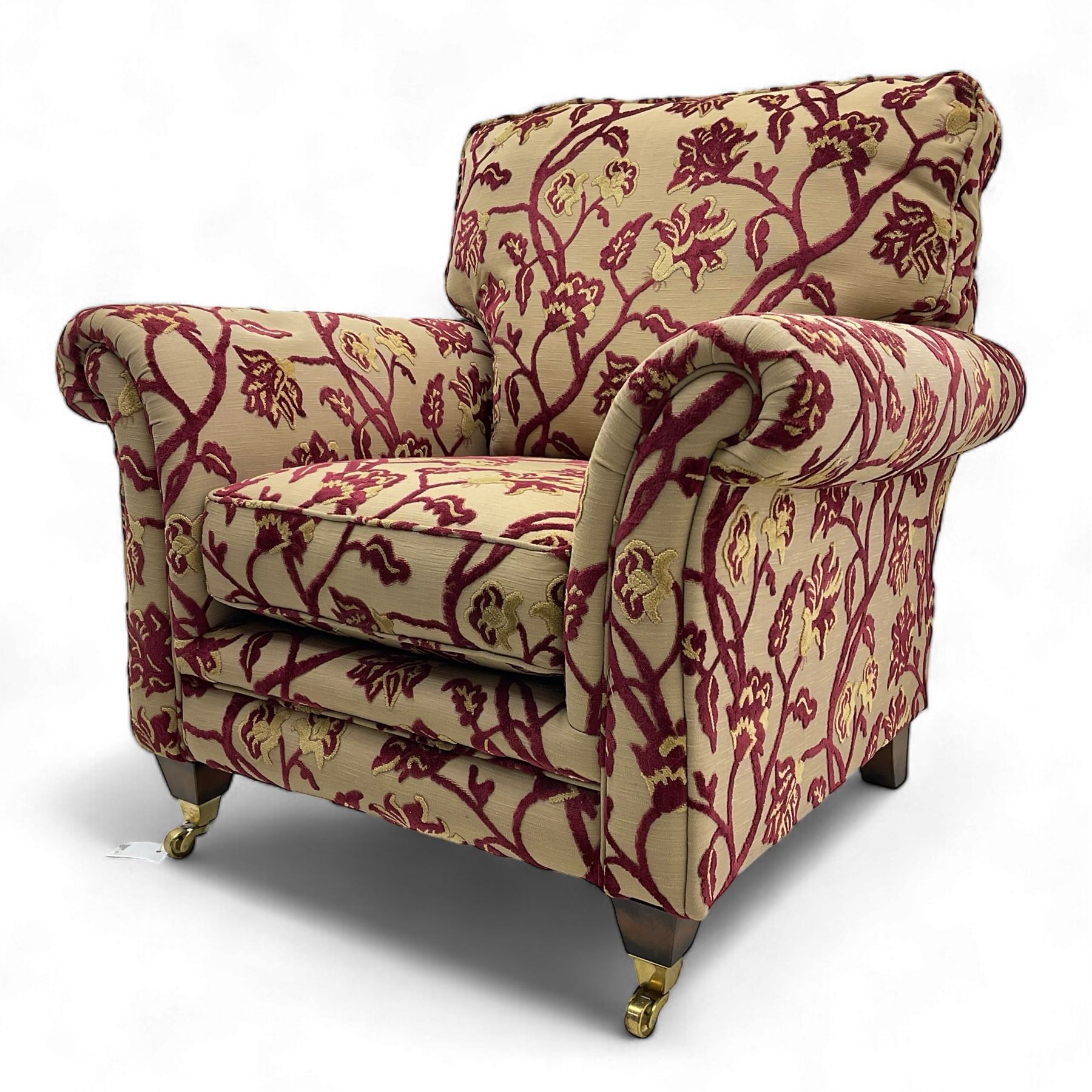 Contemporary upholstered armchair, scroll arms and loose cushions, embossed beige ground fabric with red and gold floral motifs, on tapered wooden supports with front brass castors