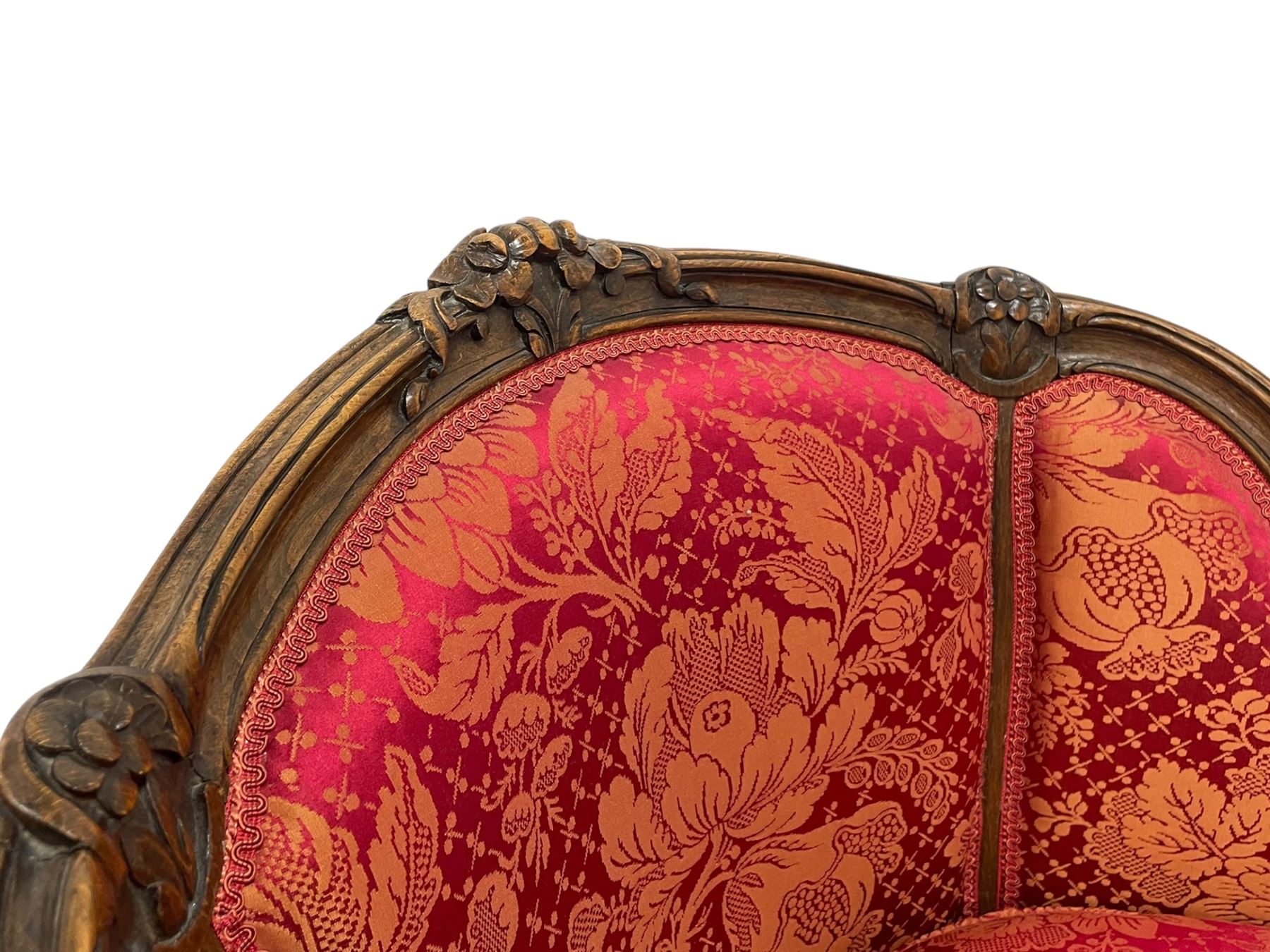 Late 20th century French design stained beech framed armchair and matching stool - the armchair with shaped and moulded frame carved with flower heads and foliage, upholstered in silk red and gold ground fabric with floral pattern, on scroll carved cabriole feet decorated with flower head carvings (W73cm, H82cm, D75cm); the footstool of concaved rectangular form with moulded frame carved with flower heads, upholstered loose cushion, on cabriole feet (70cm x 64cm, H48cm)