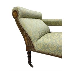 Late Victorian walnut salon settee or chaise lounge, double-ended with rolled back and curved end, upholstered in light aquamarine fabric with raised repeating lozenge pattern, decorated with laurel leaf wreaths and urns, three pierced splats carved with curled leaves, inlaid with dolphins and scrolled foliate motifs in simulated ivory and boxwood, on tapering ring turned supports with brass and ceramic castors (L166, D60, H70cm); together with matching tub-shaped armchair (W61cm, H73cm, D66cm)  