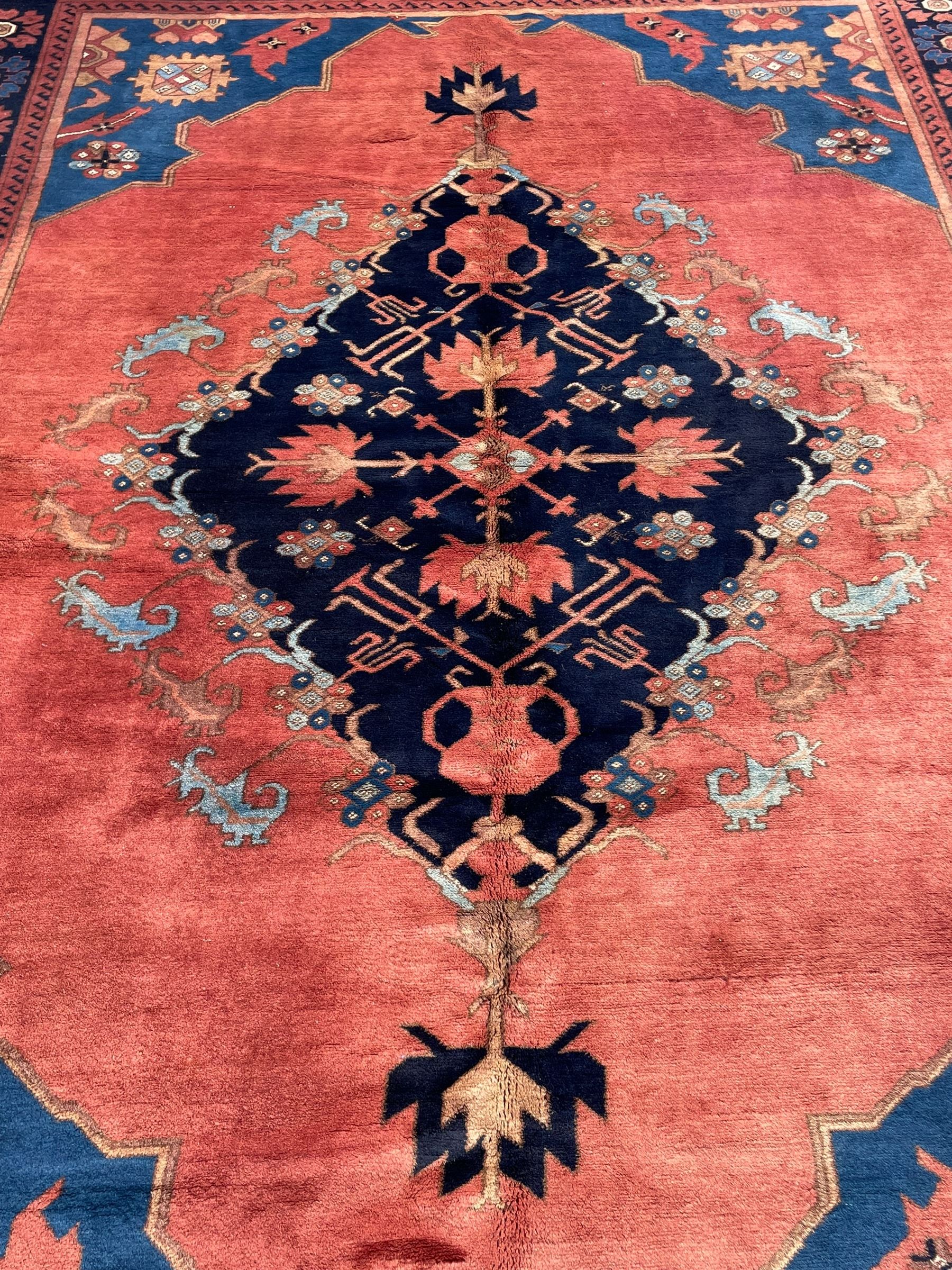 Afghan rust ground carpet, large central lozenge medallion decorated with stylised plant motifs, running water guard stripes enclosing indigo ground border decorated with stylised flower heads