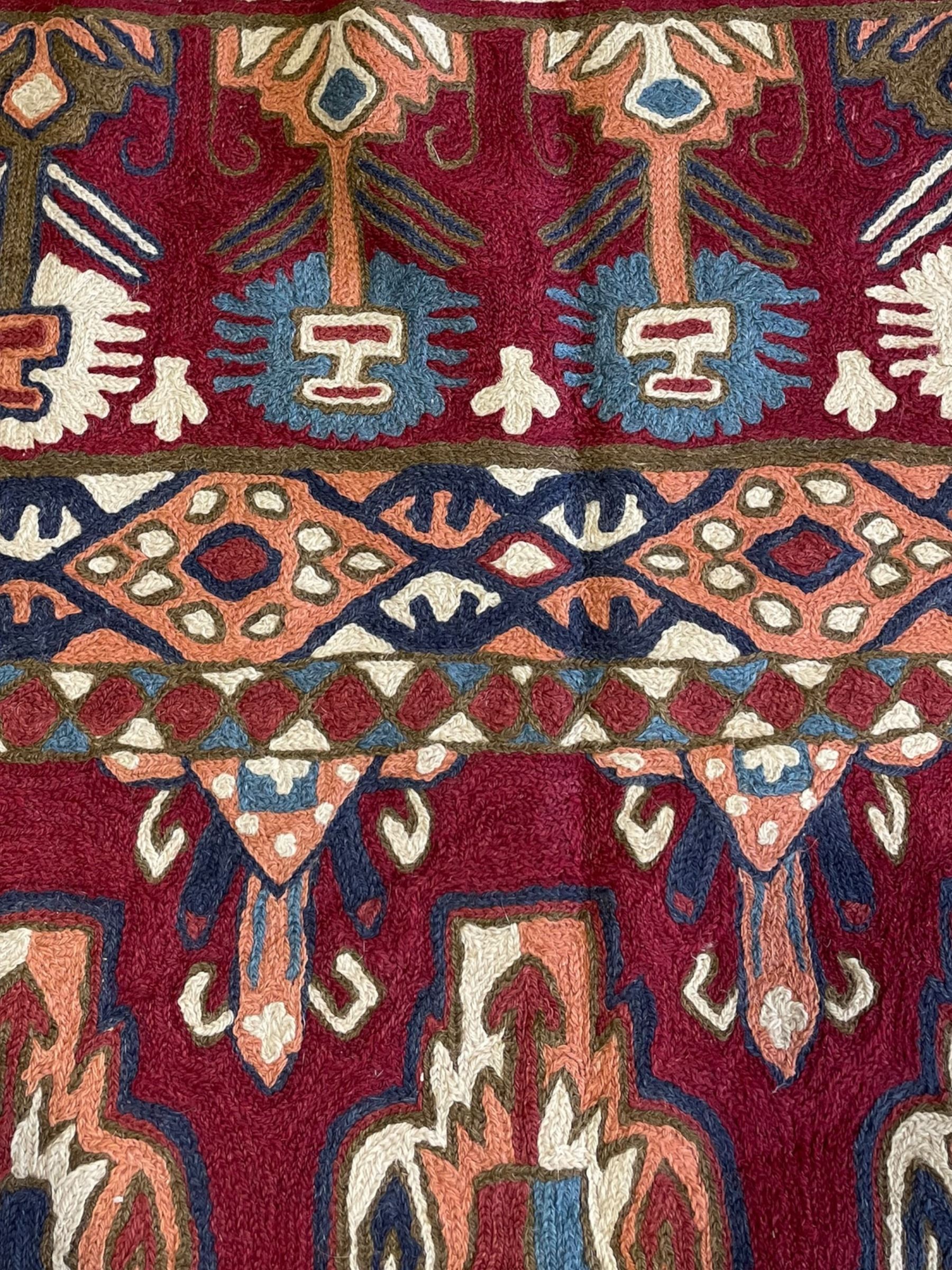 Caucasian design crewelwork hanging, crimson ground, the field decorated with geometric designs, the wide guard band with repeating stylised plant  motifs