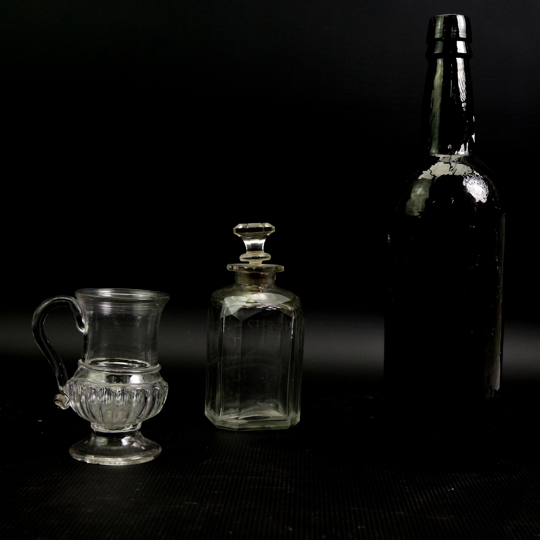 Glass coin jug, with ribbed body and inset with a George II silver 1d penny, H11cm; an 18th century Shrub decanter, circa 1785, H15.5cm; together with an 18th century English green wine bottle, H29.5cm (3)