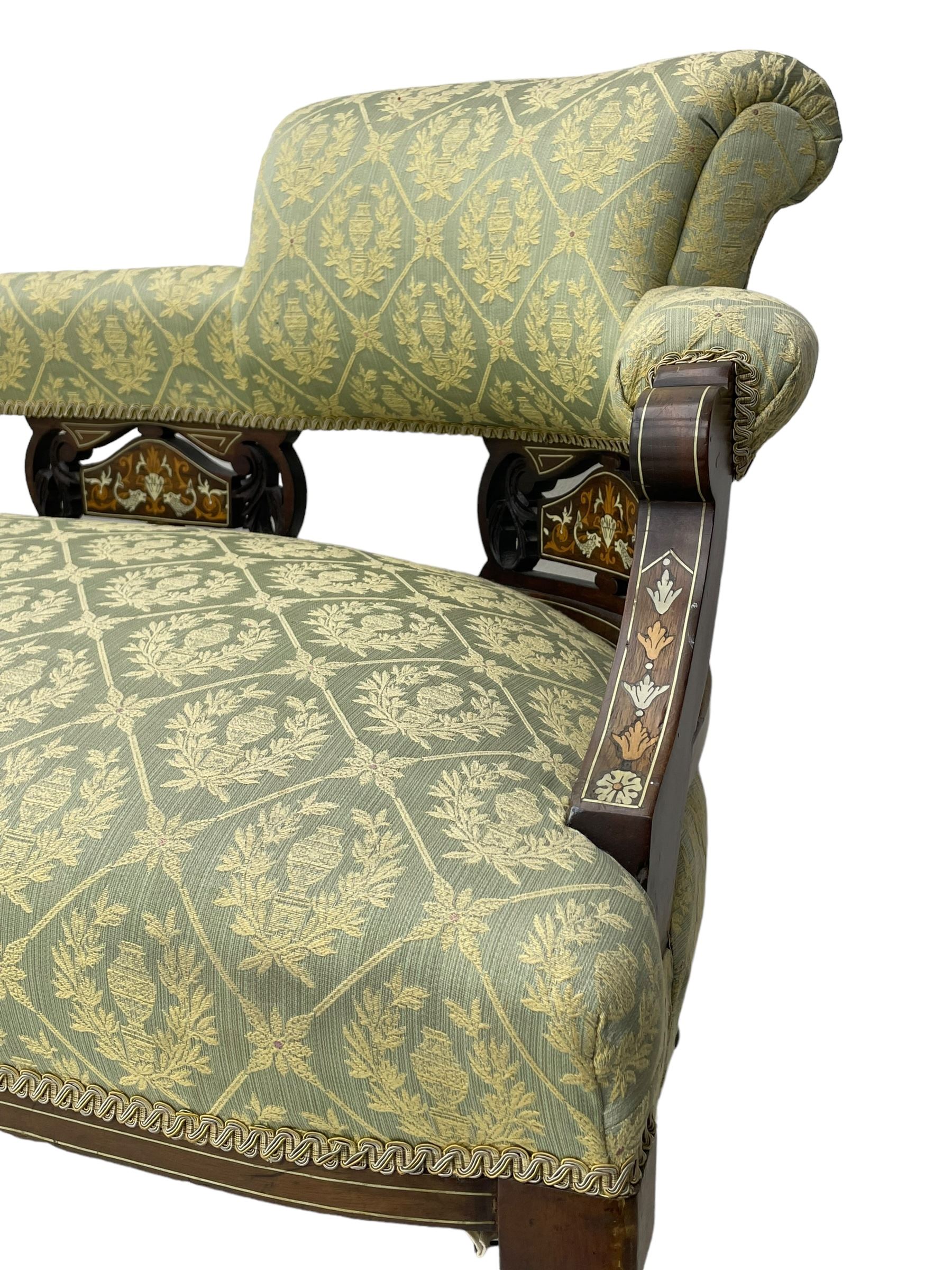 Late Victorian walnut salon settee or chaise lounge, double-ended with rolled back and curved end, upholstered in light aquamarine fabric with raised repeating lozenge pattern, decorated with laurel leaf wreaths and urns, three pierced splats carved with curled leaves, inlaid with dolphins and scrolled foliate motifs in simulated ivory and boxwood, on tapering ring turned supports with brass and ceramic castors (L166, D60, H70cm); together with matching tub-shaped armchair (W61cm, H73cm, D66cm)  