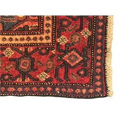 Northwest Persian Senneh crimson ground rug, central ivory lozenge medallion with geometric motifs, framed by matching spandrels, the surrounding field densely filled with stylised floral and foliate patterns, guarded border with repeating geometric and foliate motifs