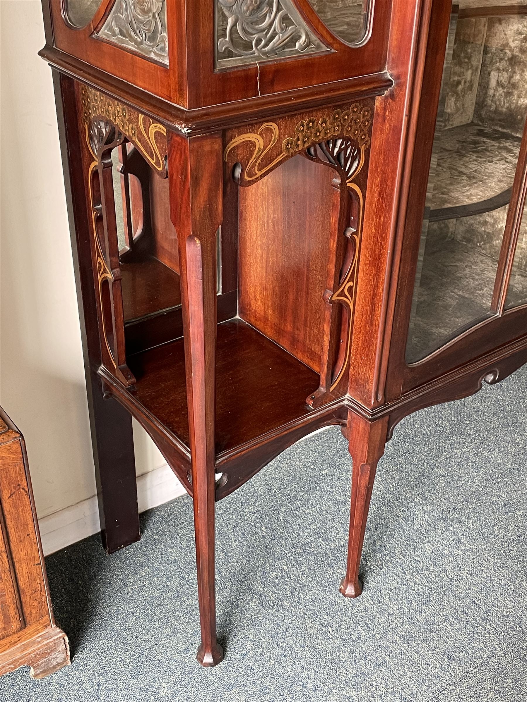 Art Nouveau period inlaid mahogany display cabinet, raised shaped and moulded pediment over projecting moulded cornices, the upper frieze inlaid with trailing branches and tulips, single astragal and bevel glazed door enclosed velvet lined interior fitted with shelves, flanked by curved glass panes decorated with pierced metal foliate spandrels, lower flanking shelves with mirror backs enclosed within shaped and pierced rails inlaid with flower heads, on tapering octagonal supports terminating to compressed pad feet, the lock stamped 'Salmon Bros, London' 