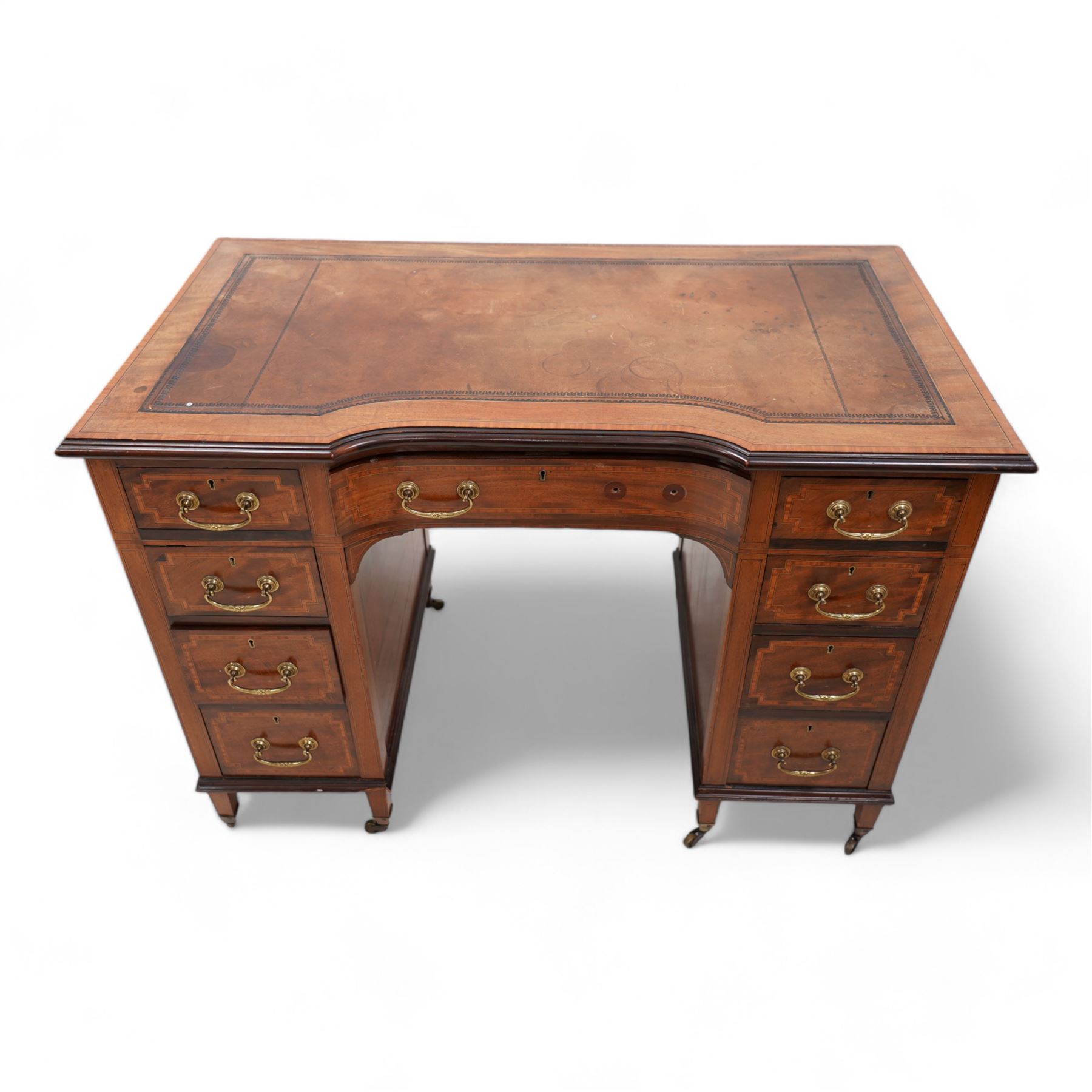 Edwardian inlaid mahogany reverse break bowfront desk, moulded satinwood banded top with inset leather writing surface, fitted with nine drawers, on square tapering feet with brass cups and castors 