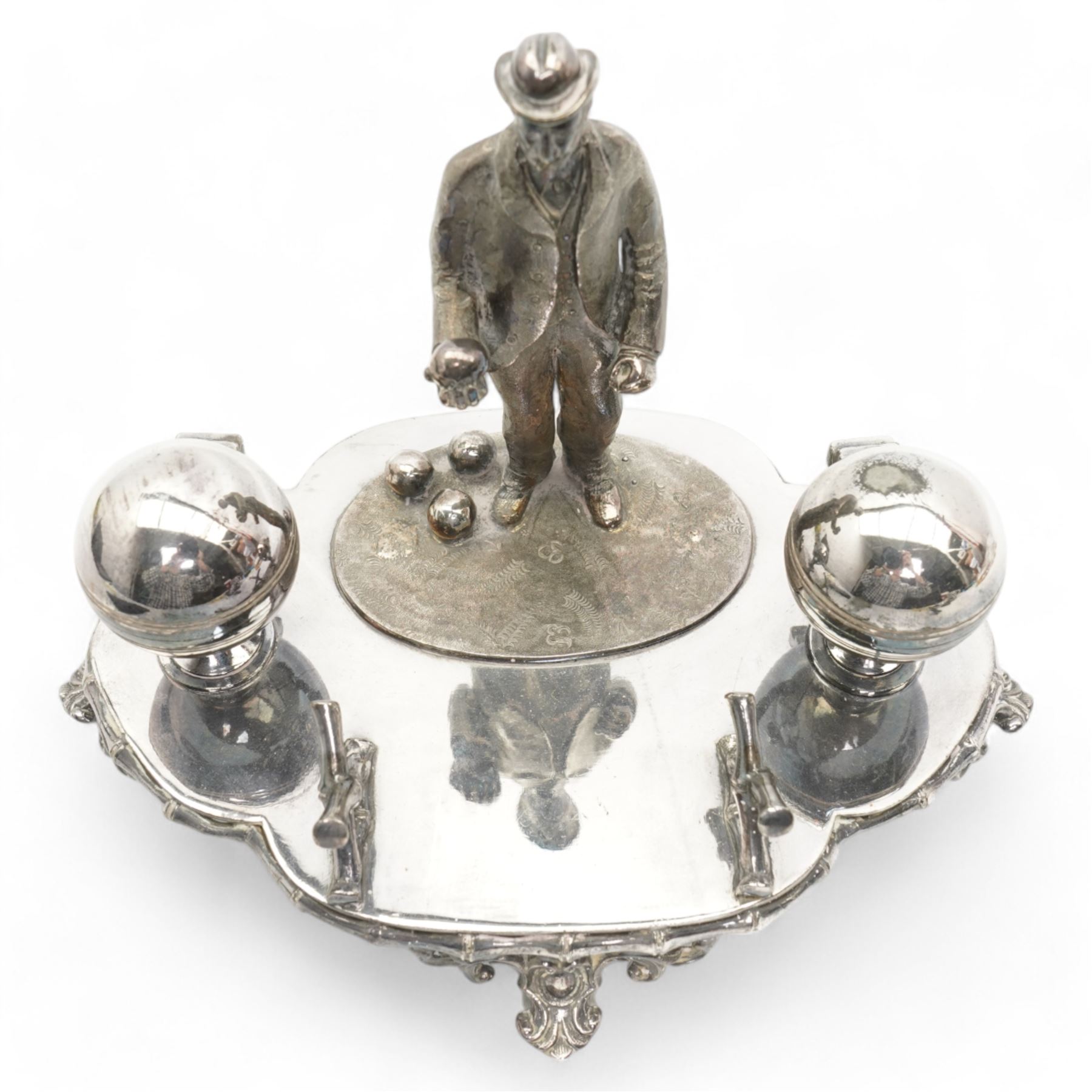 Victorian silver-plated inkstand by James Dixon & Sons, the quatrefoil base surmounted with a figure of a lawn bowler stood upon an oval grass base, with three lawn bowls by his feet, the inkwells formed as two bowls, each with hinged covers and silver-plated liners, bamboo moulded pen rest and gallery, supported by four pierced and splayed feet, L22cm x H17cm