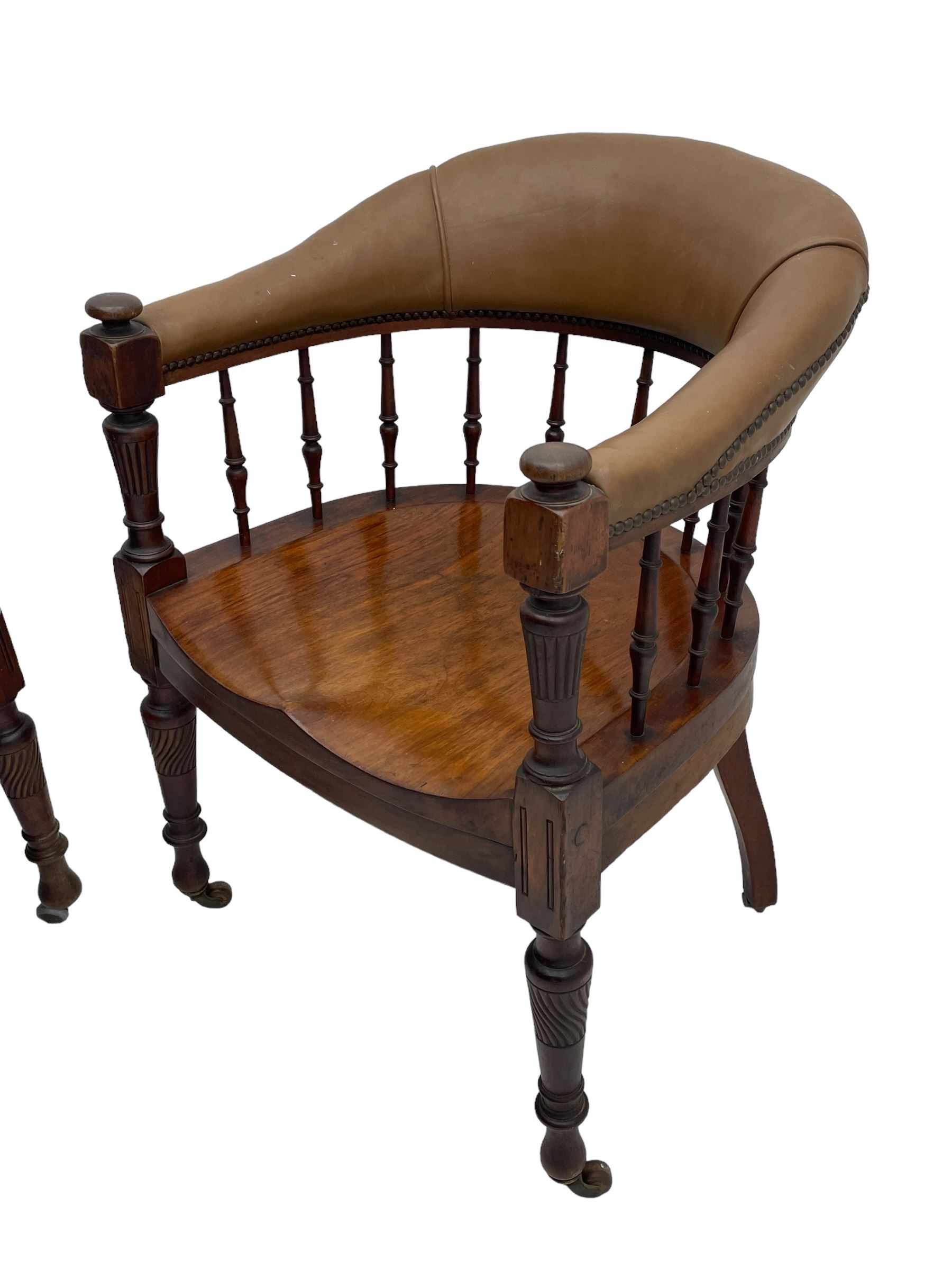 Pair of late Victorian walnut tub-shaped elbow chairs, the cushioned cresting rail upholstered in leather on spindle turned supports, dished saddle seat on turned supports